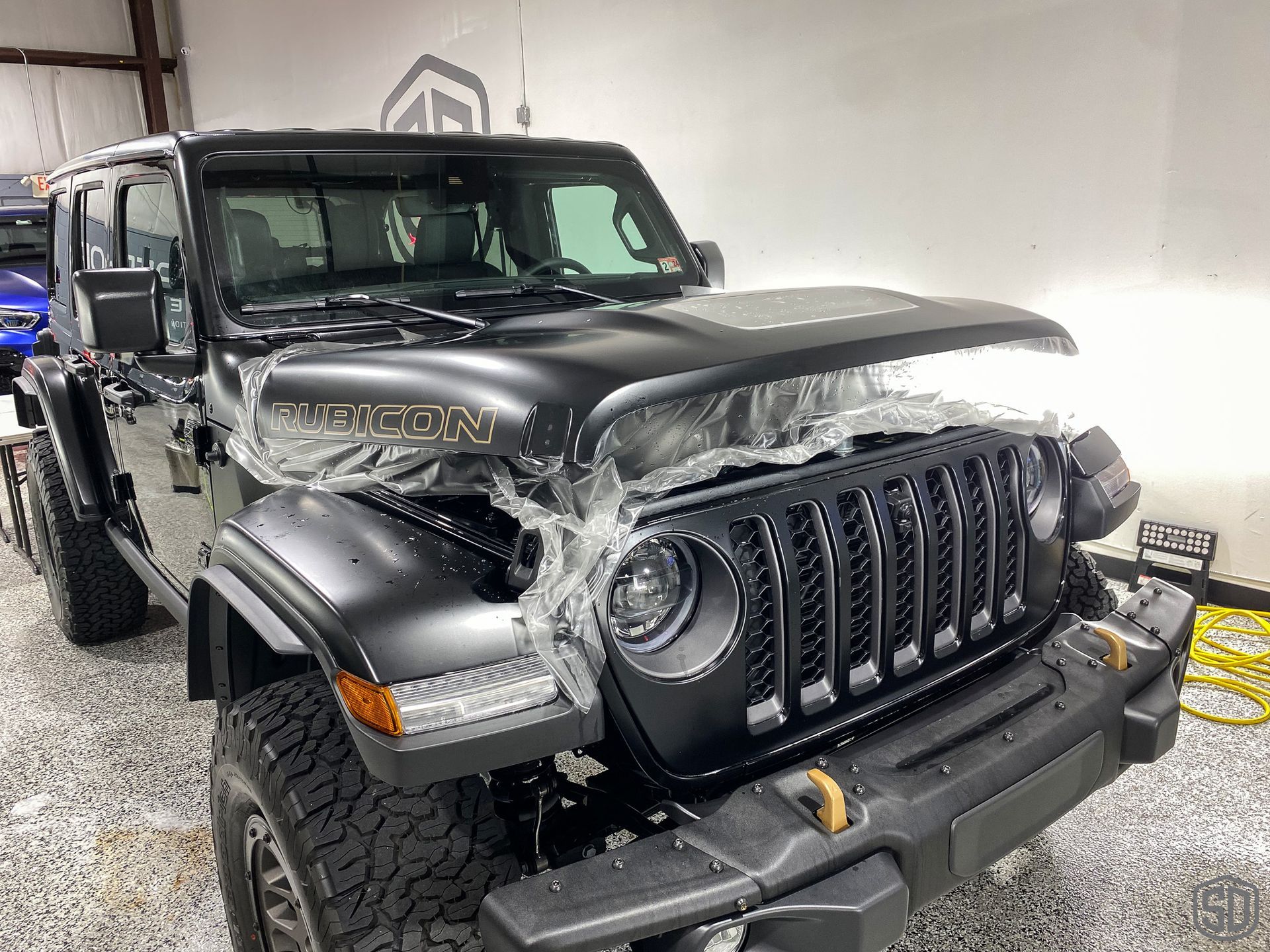 A black jeep wrangler is wrapped in plastic and sitting in a garage.