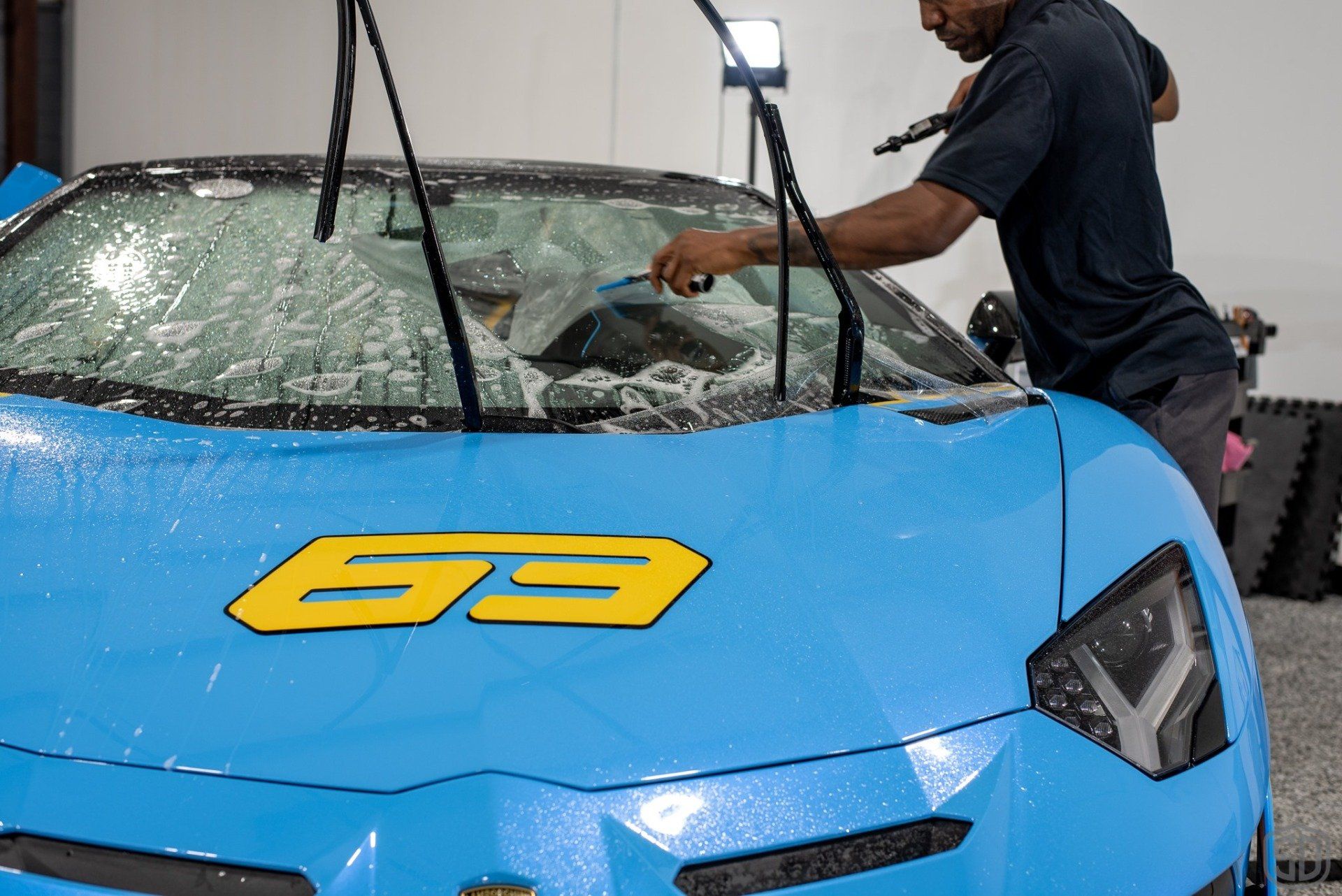 A man is cleaning the windshield of a blue sports car.