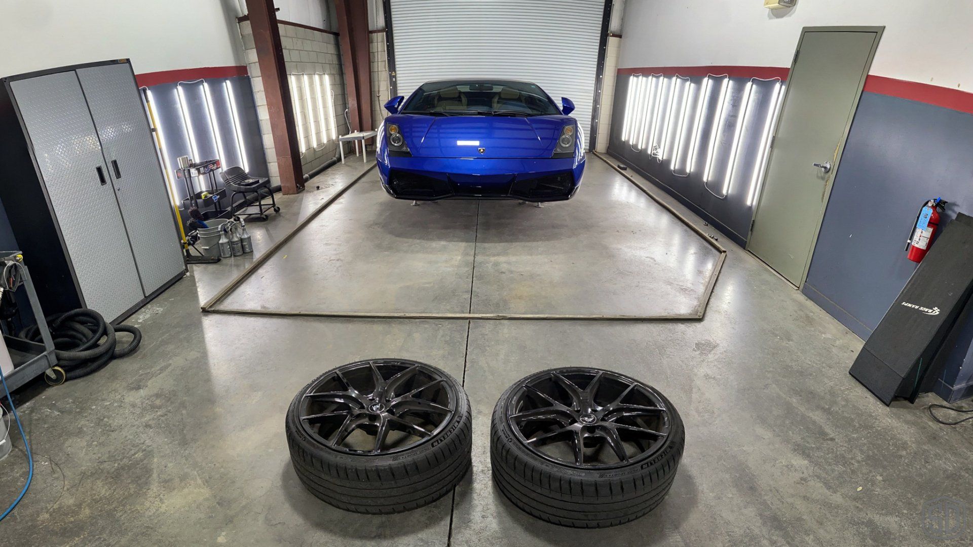 A blue sports car is parked in a garage next to two tires.