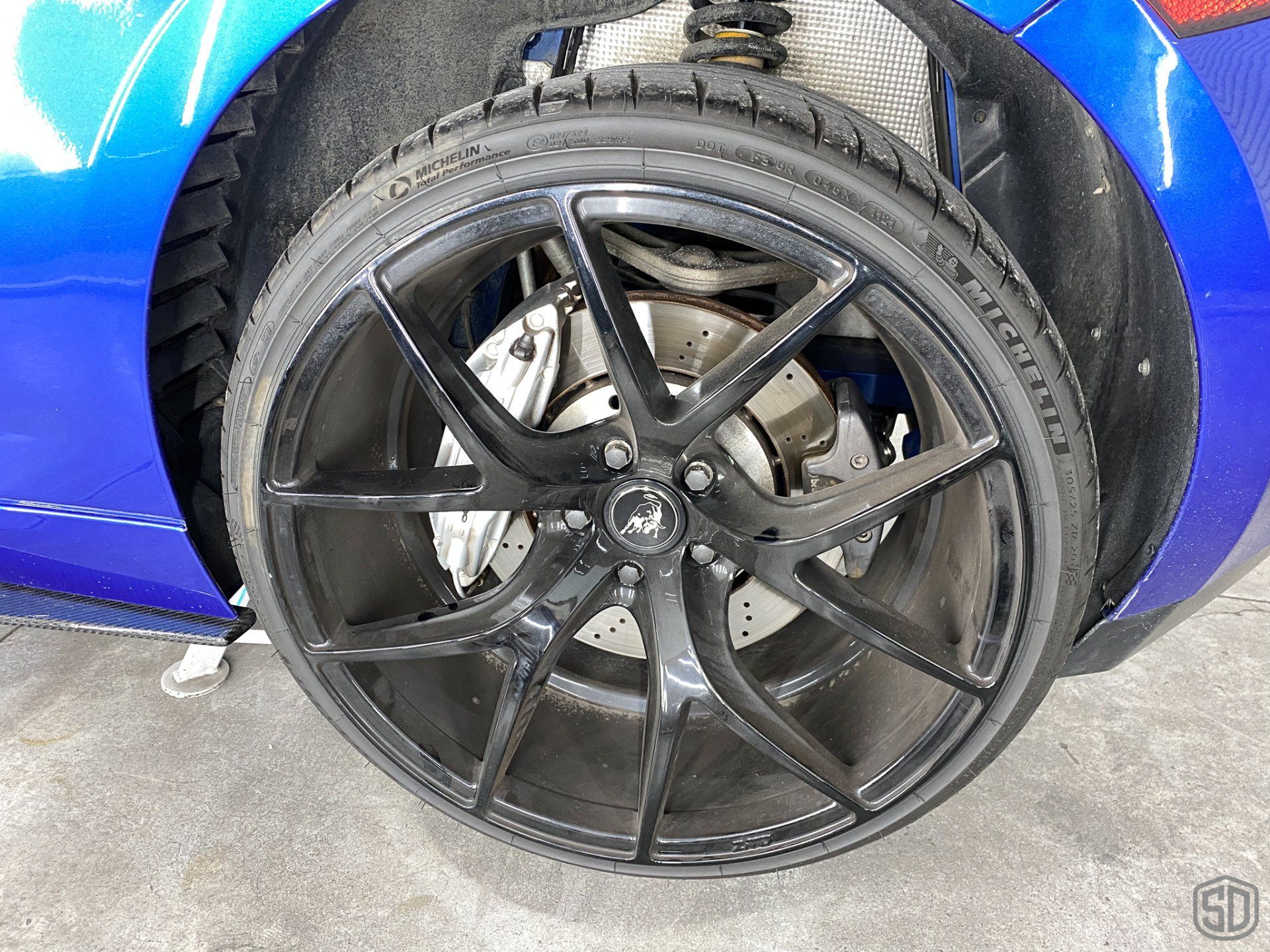 A blue sports car with black wheels and tires is parked on the side of the road.