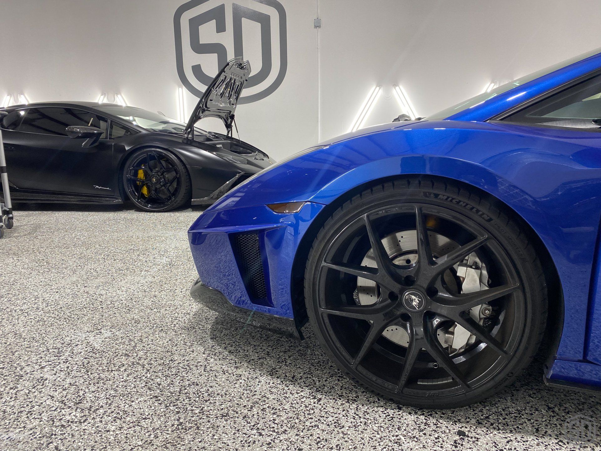 A blue sports car is parked next to a black sports car in a garage.
