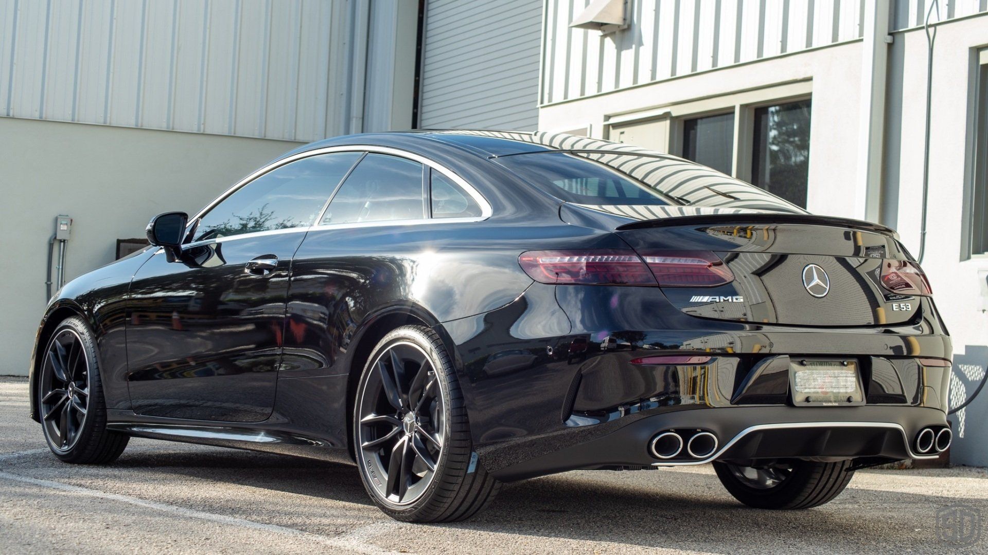 A black mercedes benz e class coupe is parked in front of a building.