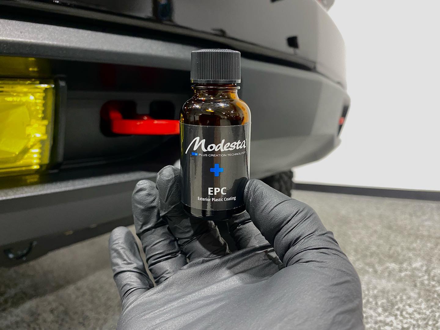 A person is holding a bottle of polish in front of a car.
