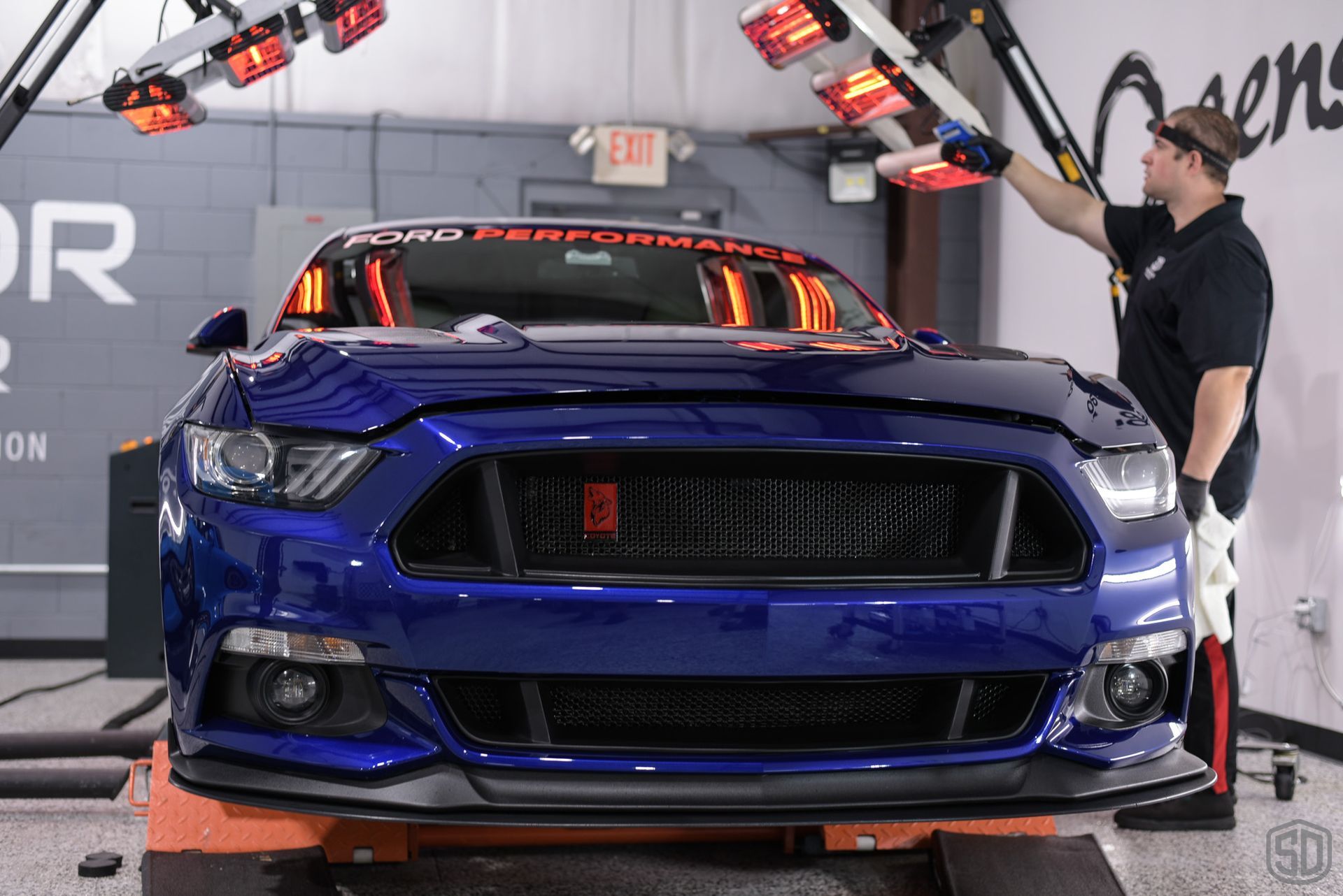 A man is working on a blue ford mustang in a garage.