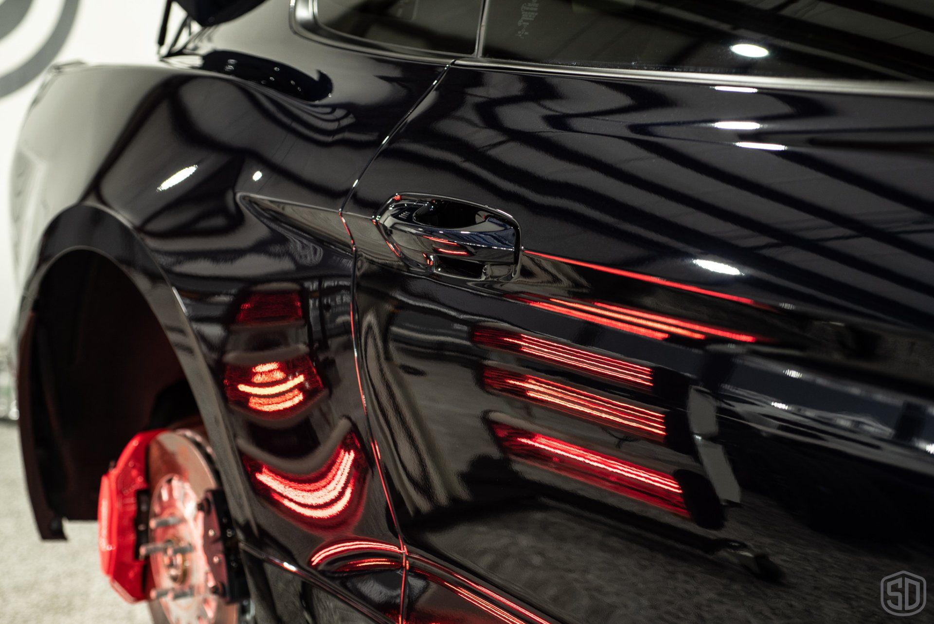 A black car with red brake calipers is parked in a garage.