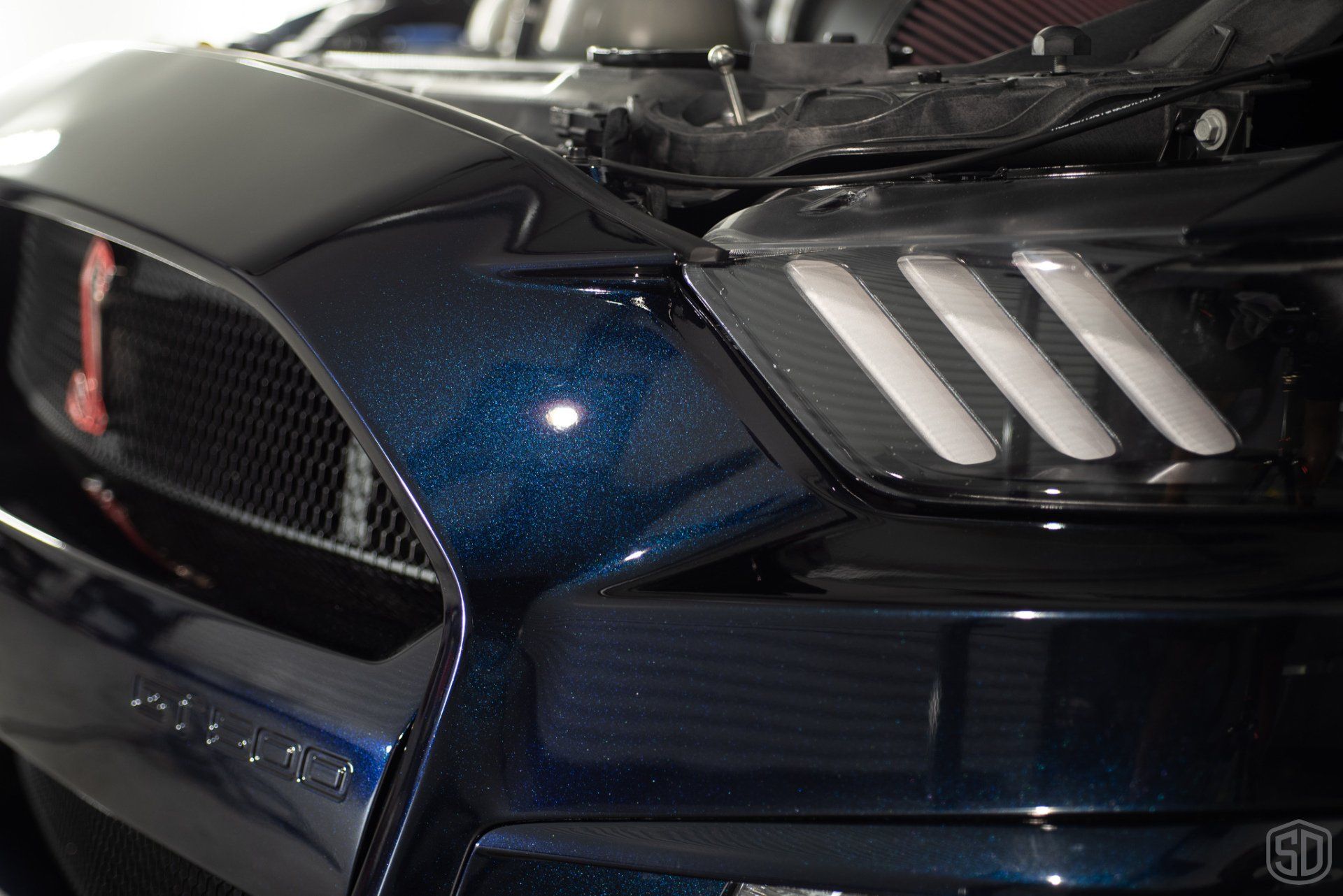 A close up of the front of a blue ford mustang with the hood open.