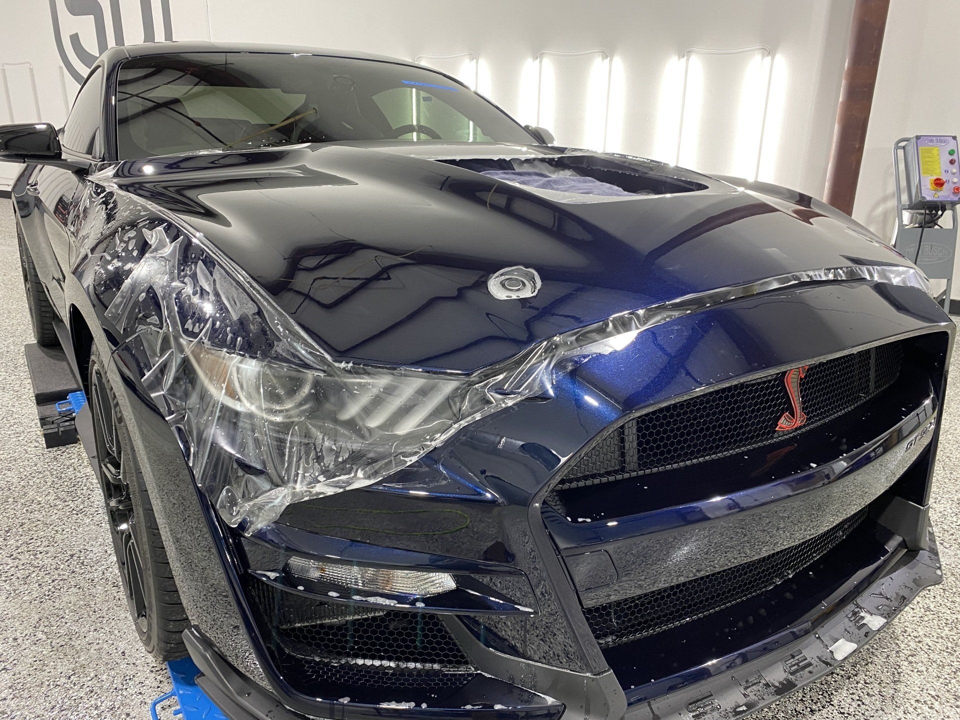 A black ford mustang is wrapped in plastic in a garage.