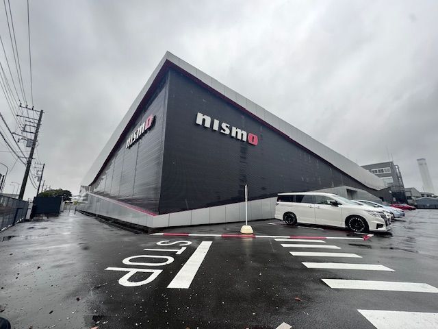 A white car is parked in front of a building that says nismo