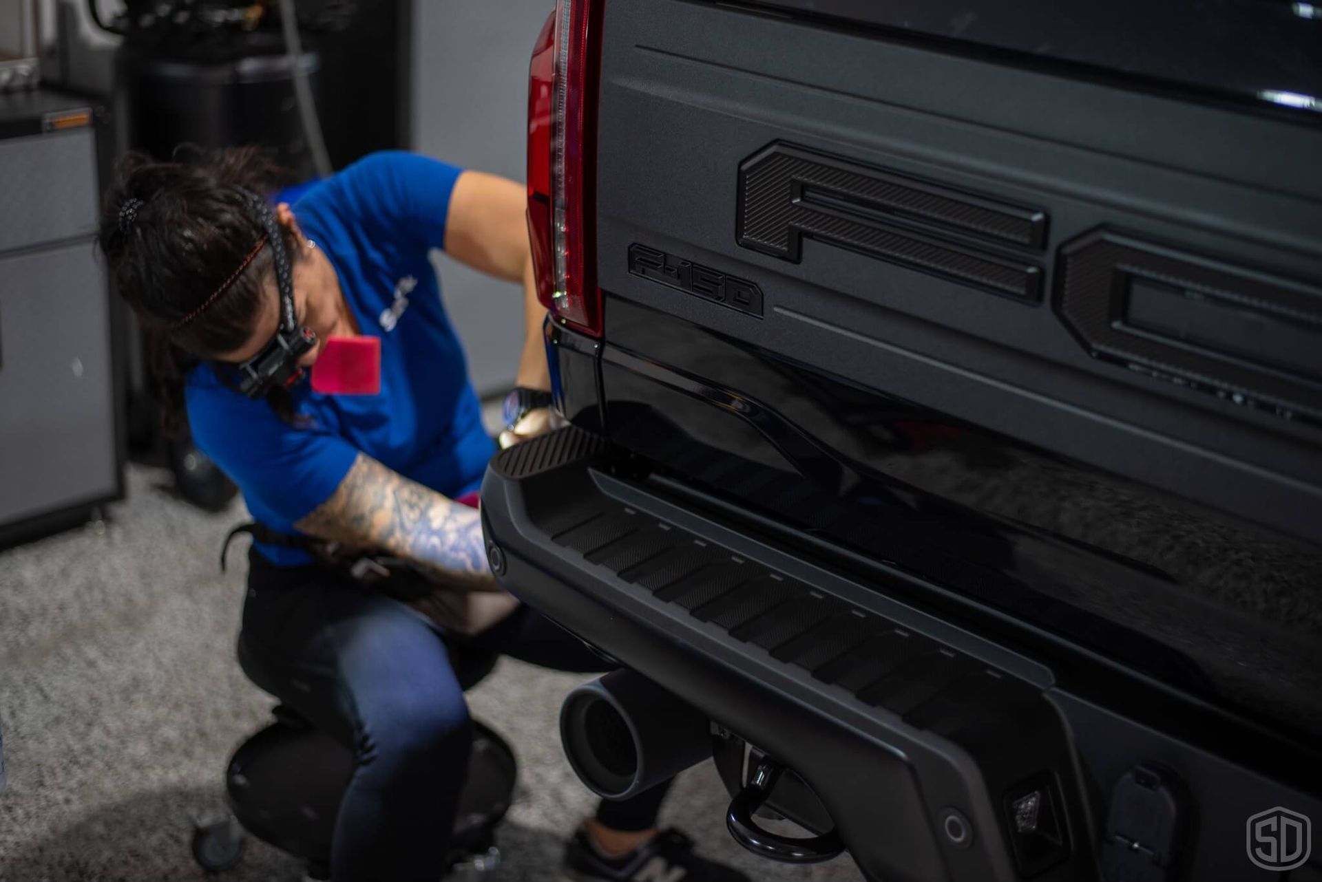A woman is cleaning the back of a black truck.