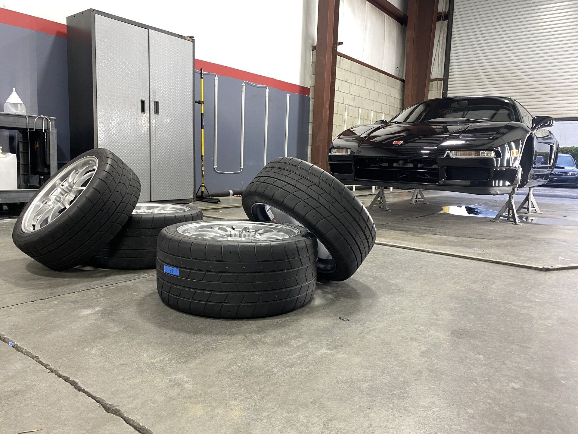 A black car is parked in a garage next to a pile of tires.
