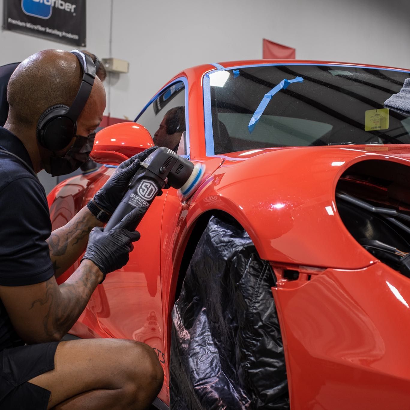 A man wearing headphones is polishing a red car