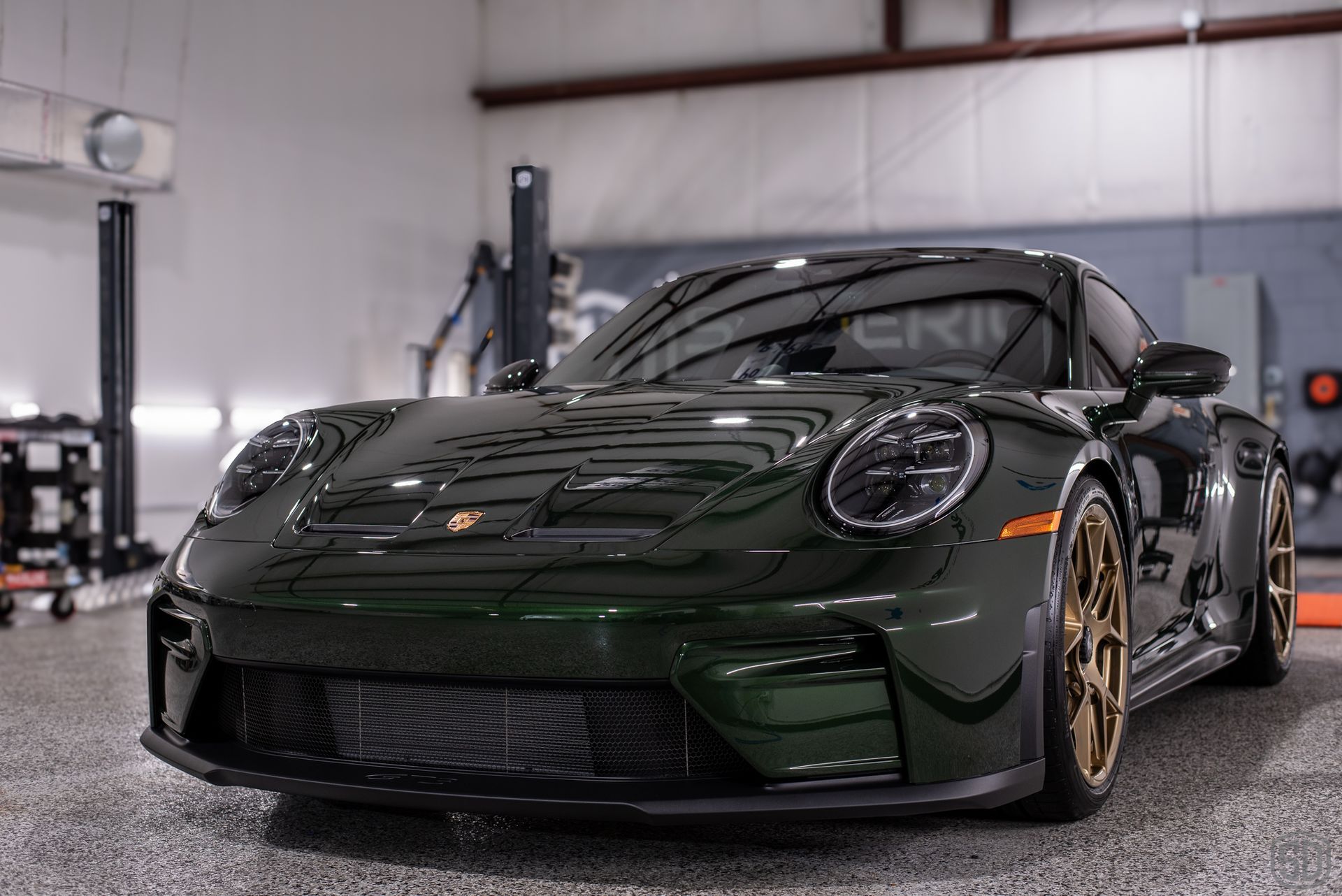 Dark green Porsche 911 in a garage, gold wheels.