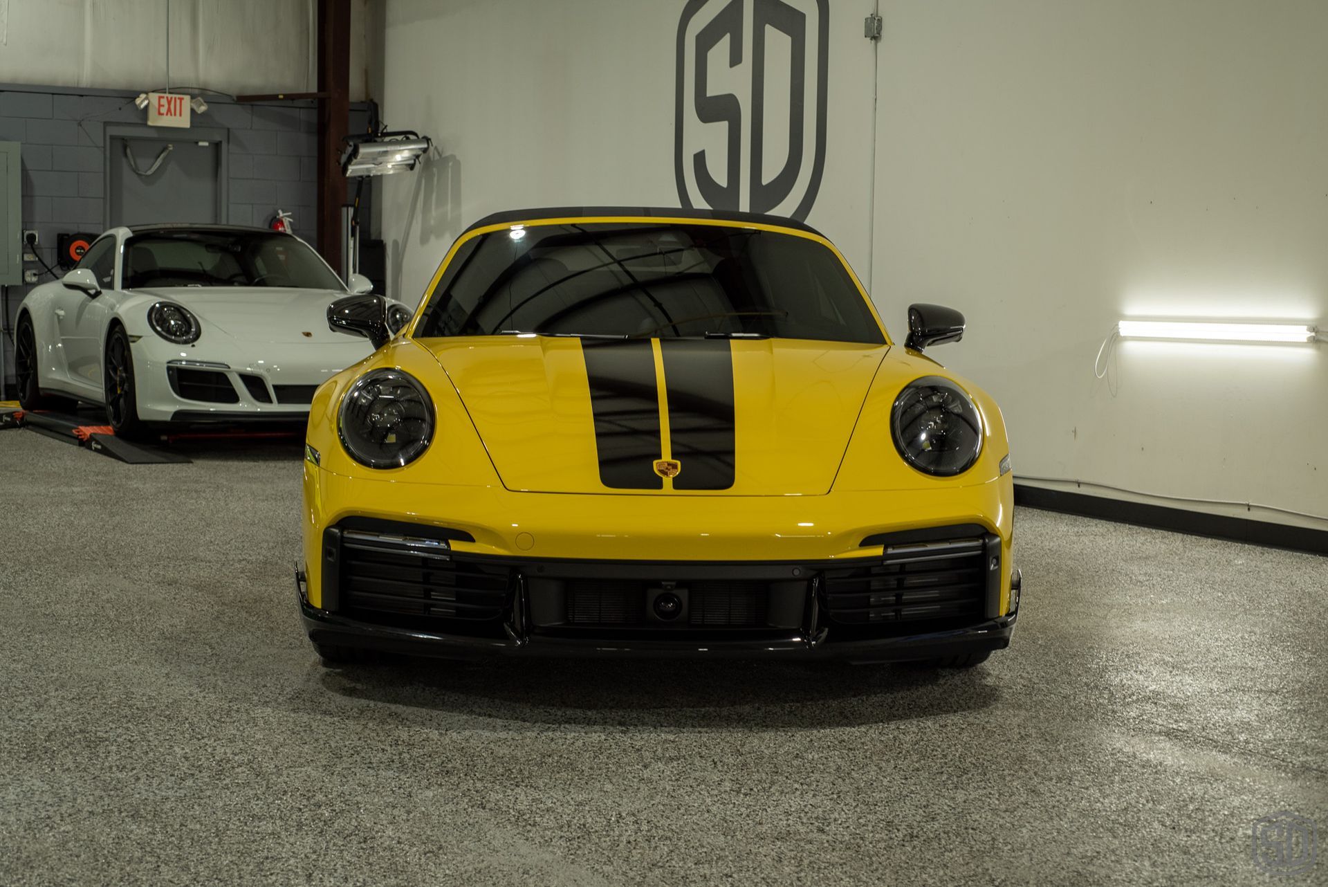 A yellow sports car is parked in a garage next to a white sports car.