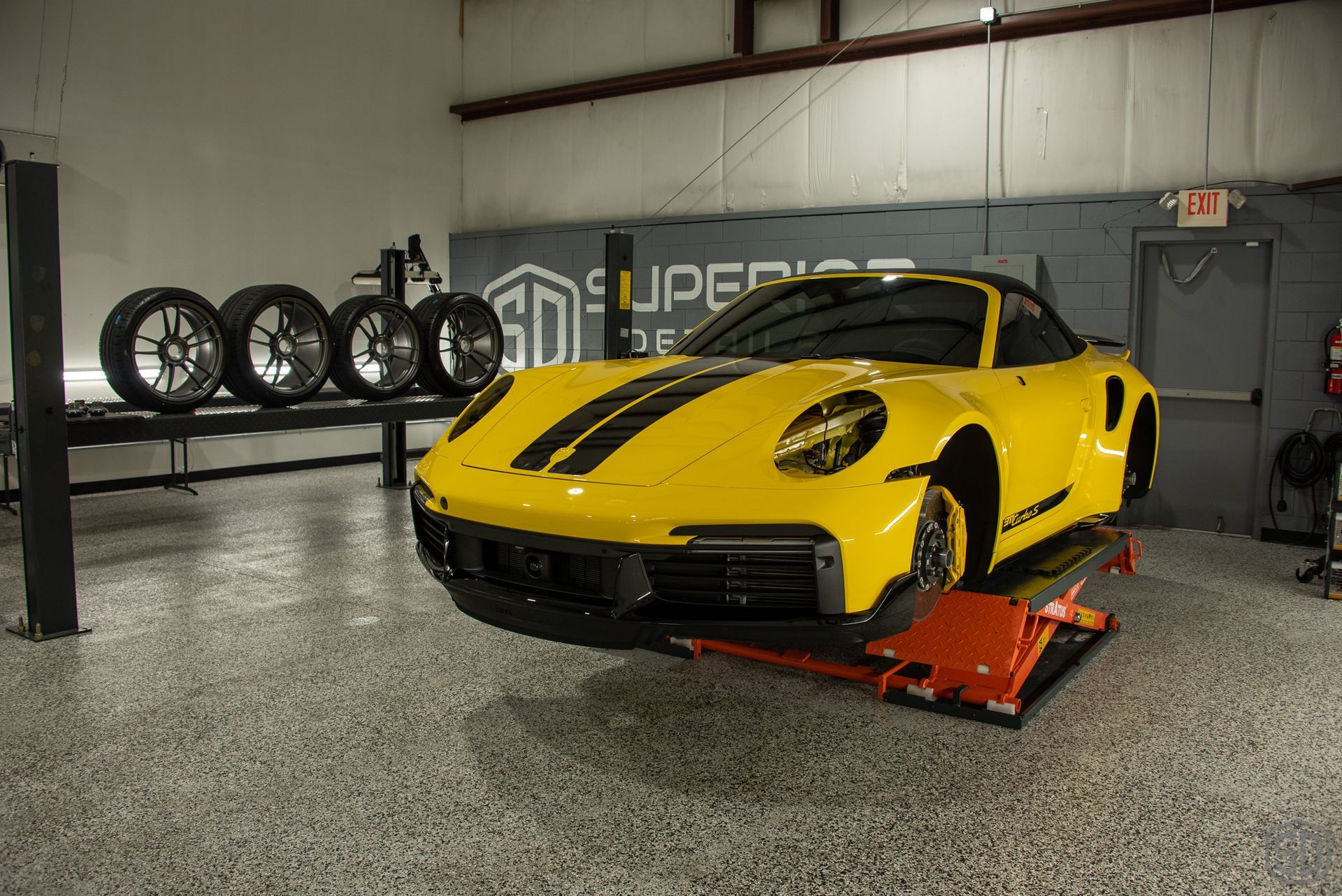 A yellow sports car is sitting on a lift in a garage.