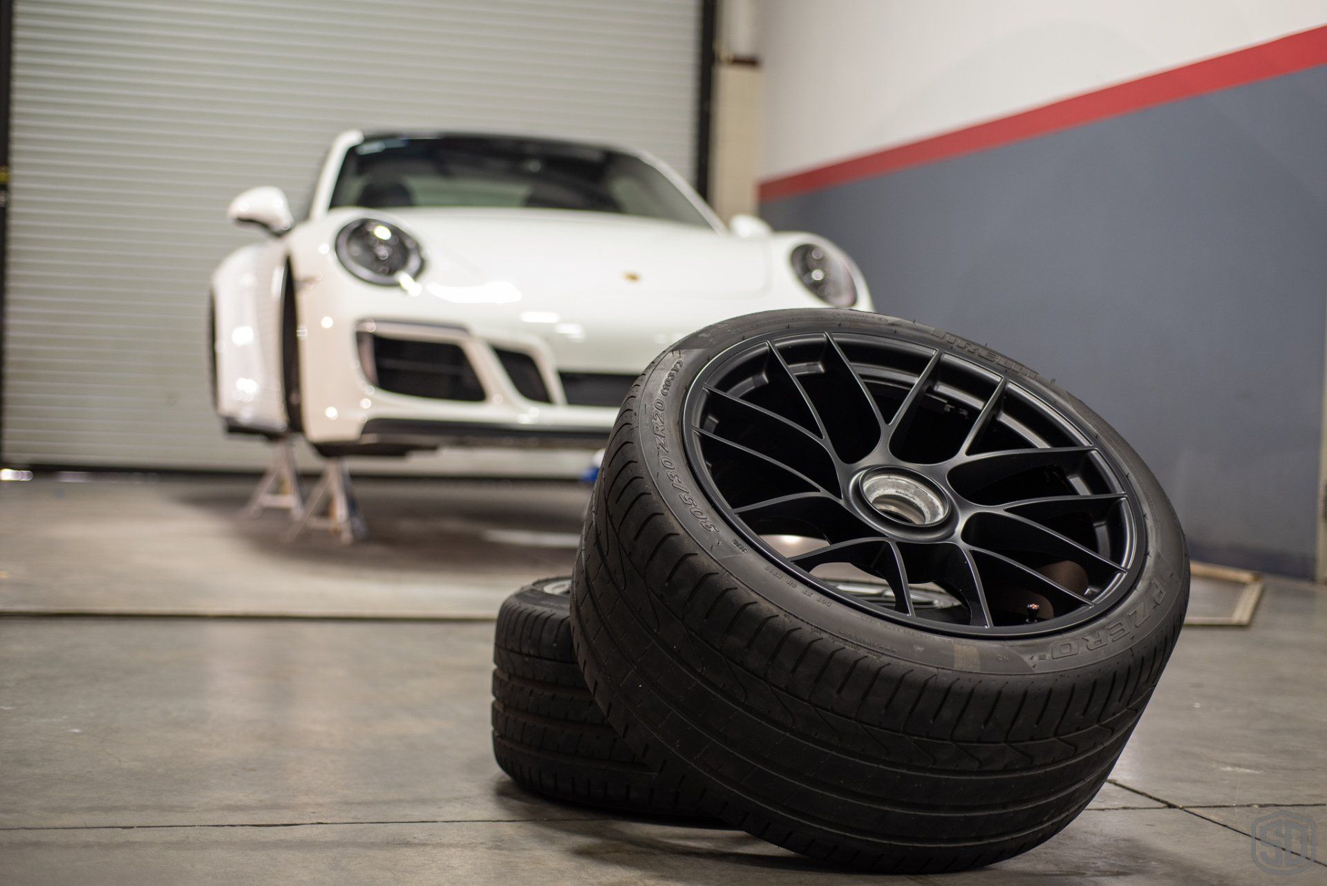 A white porsche is parked in a garage next to a stack of tires.