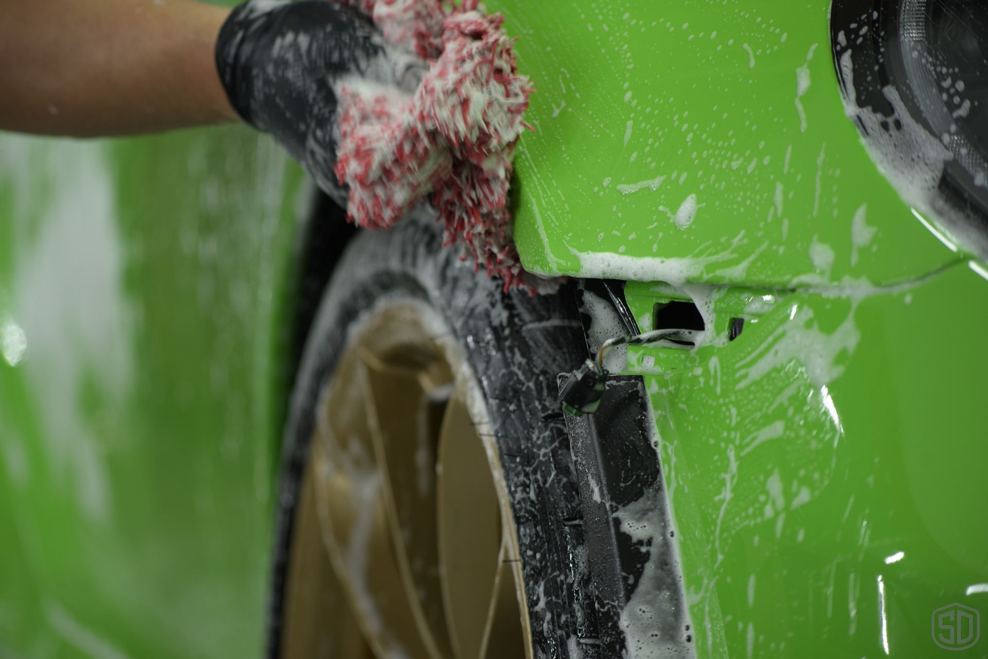 A person is washing a green car with a sponge.