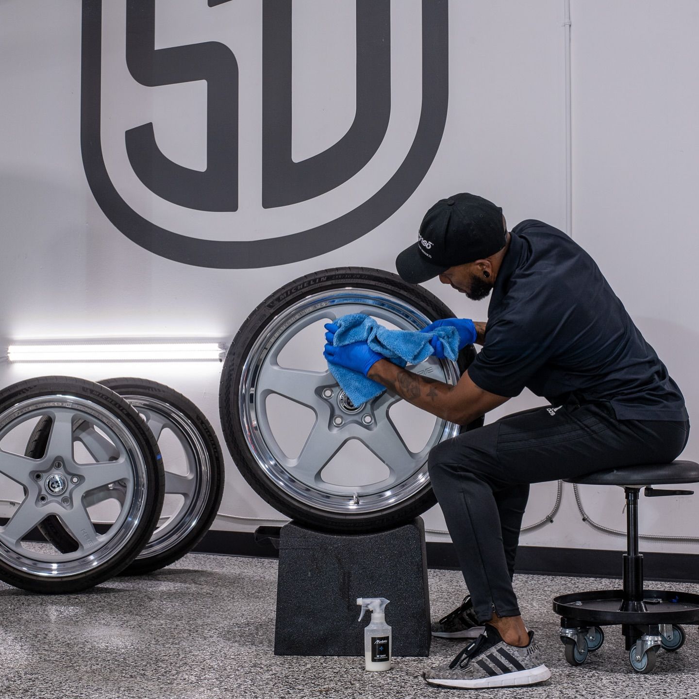 A man is sitting on a stool cleaning a wheel with a towel.