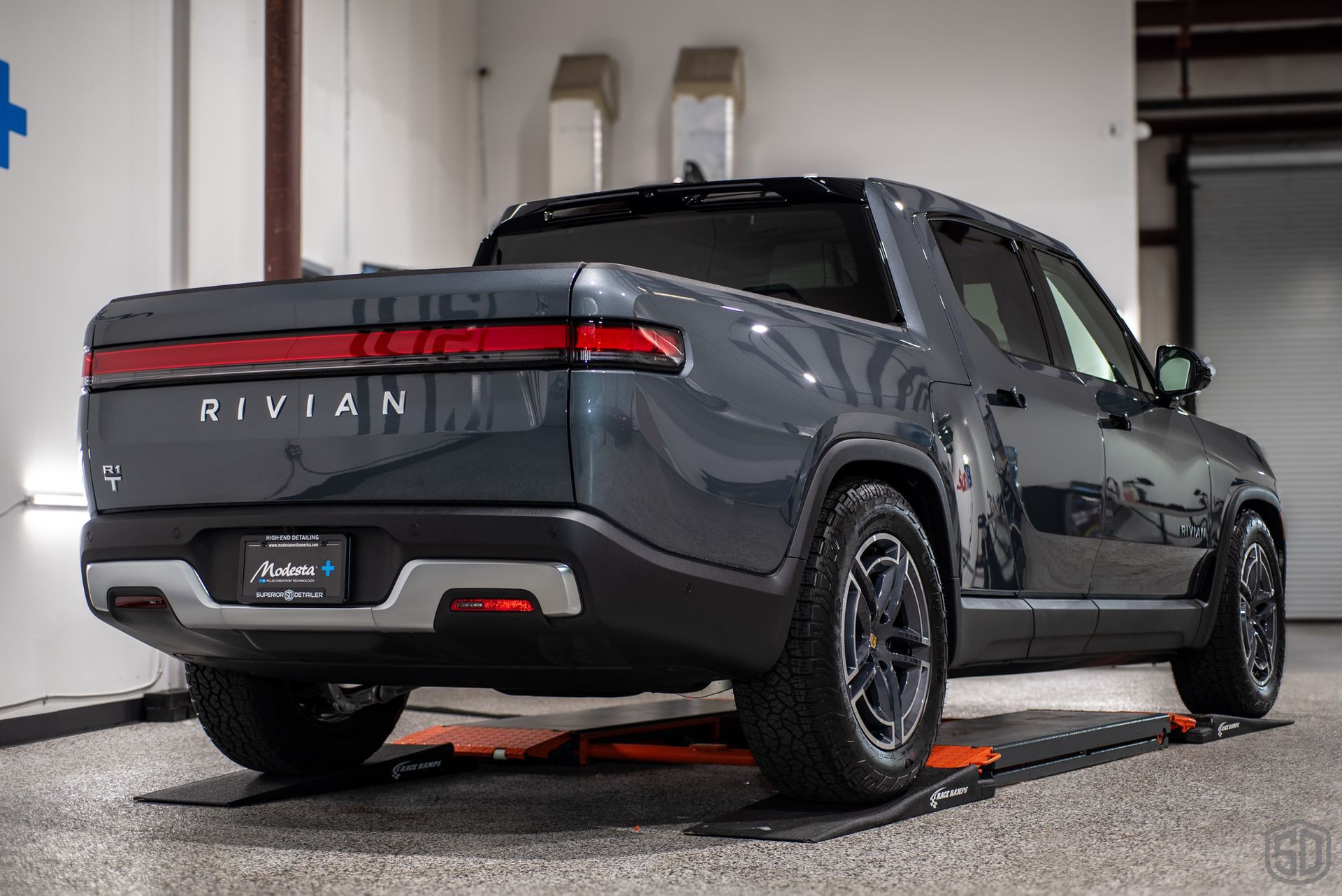 The rear end of a gray Rivian R1T truck is shown parked in a garage.