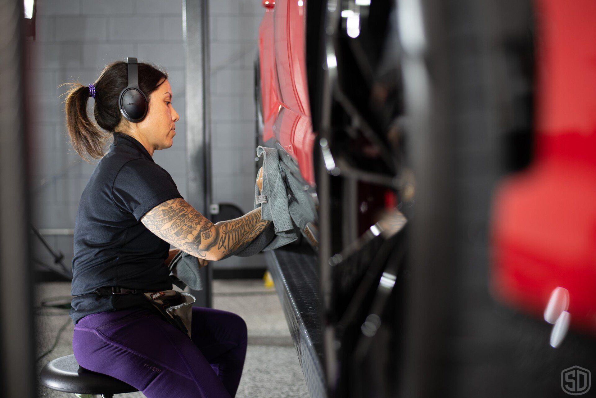 A woman is sitting on a stool cleaning a car with a cloth.