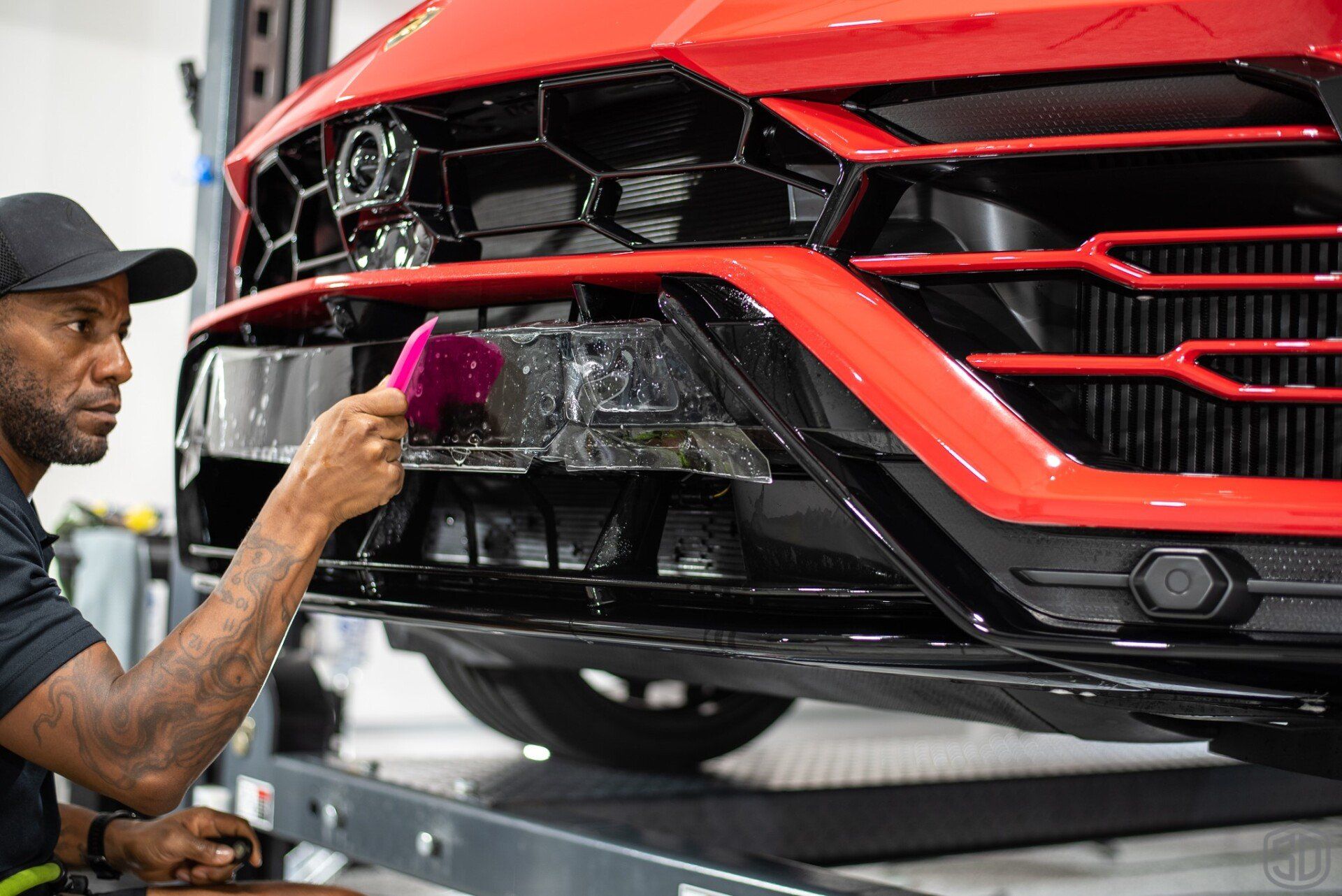 A man is applying a protective film to the front of a red car.