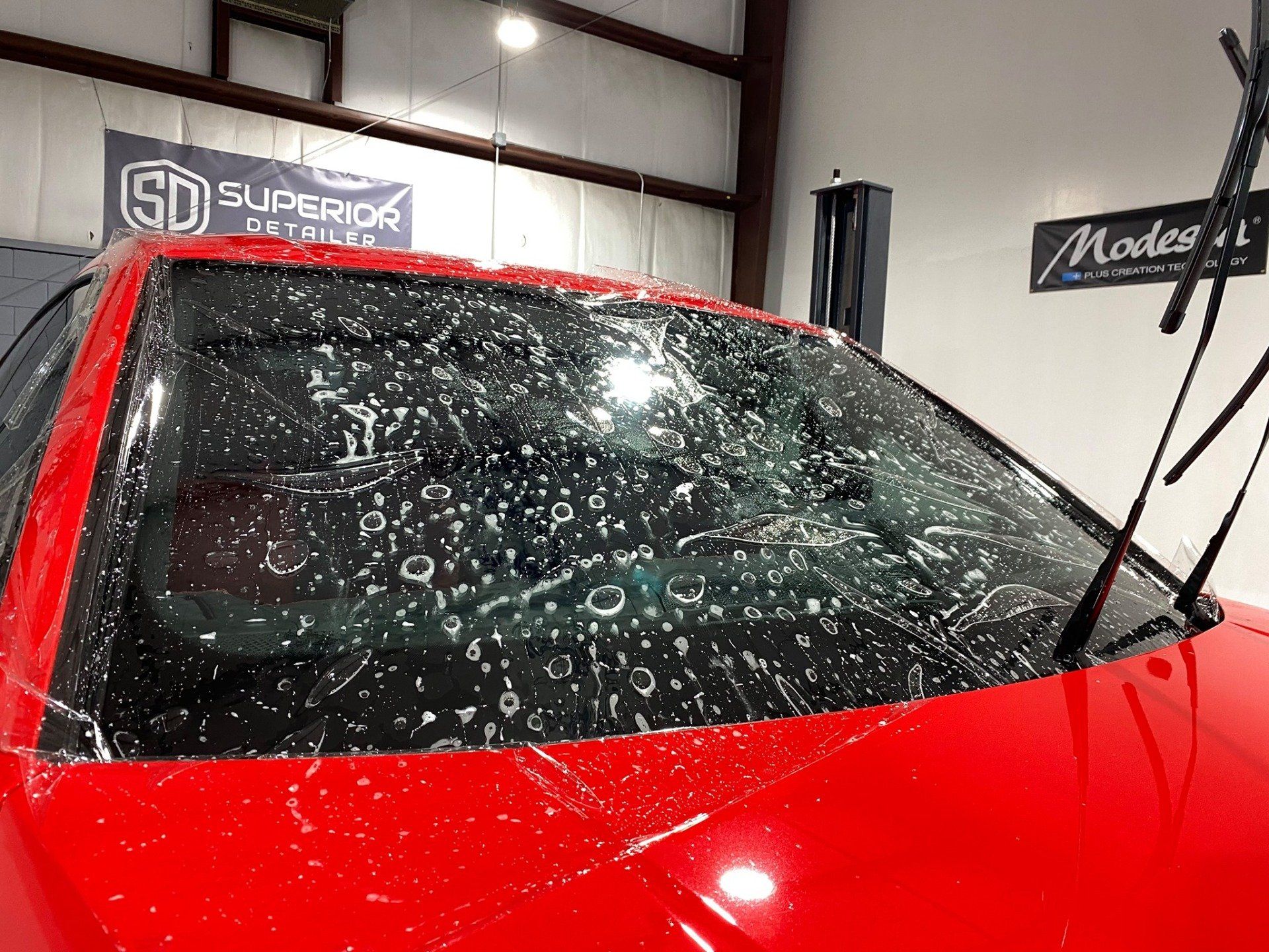 A red car with a dirty windshield is sitting in a garage.