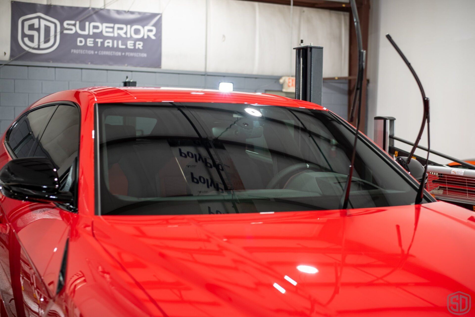 A red car is parked in a garage next to a sign that says superior detailer.