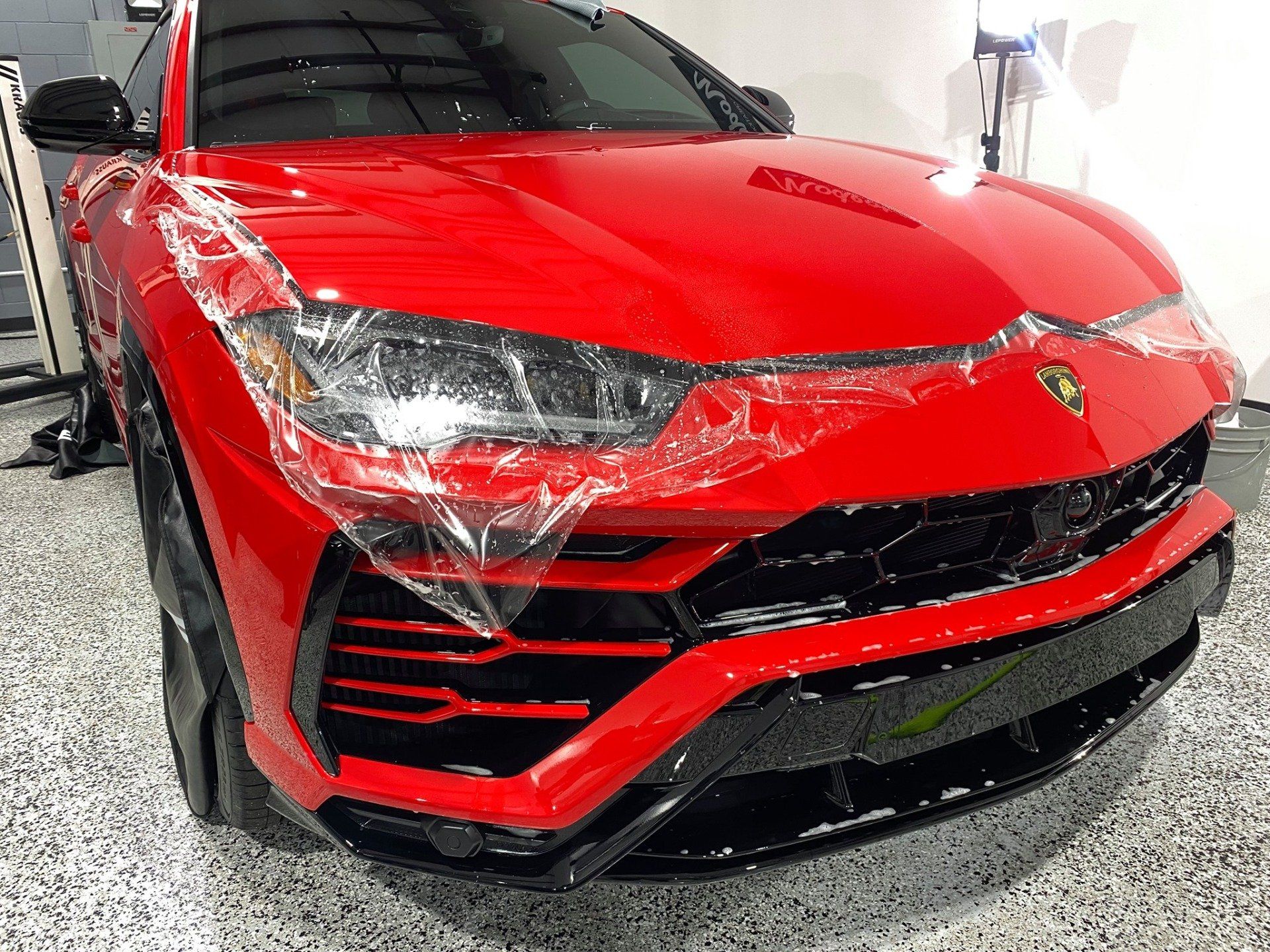 A red lamborghini urus is wrapped in plastic in a garage.