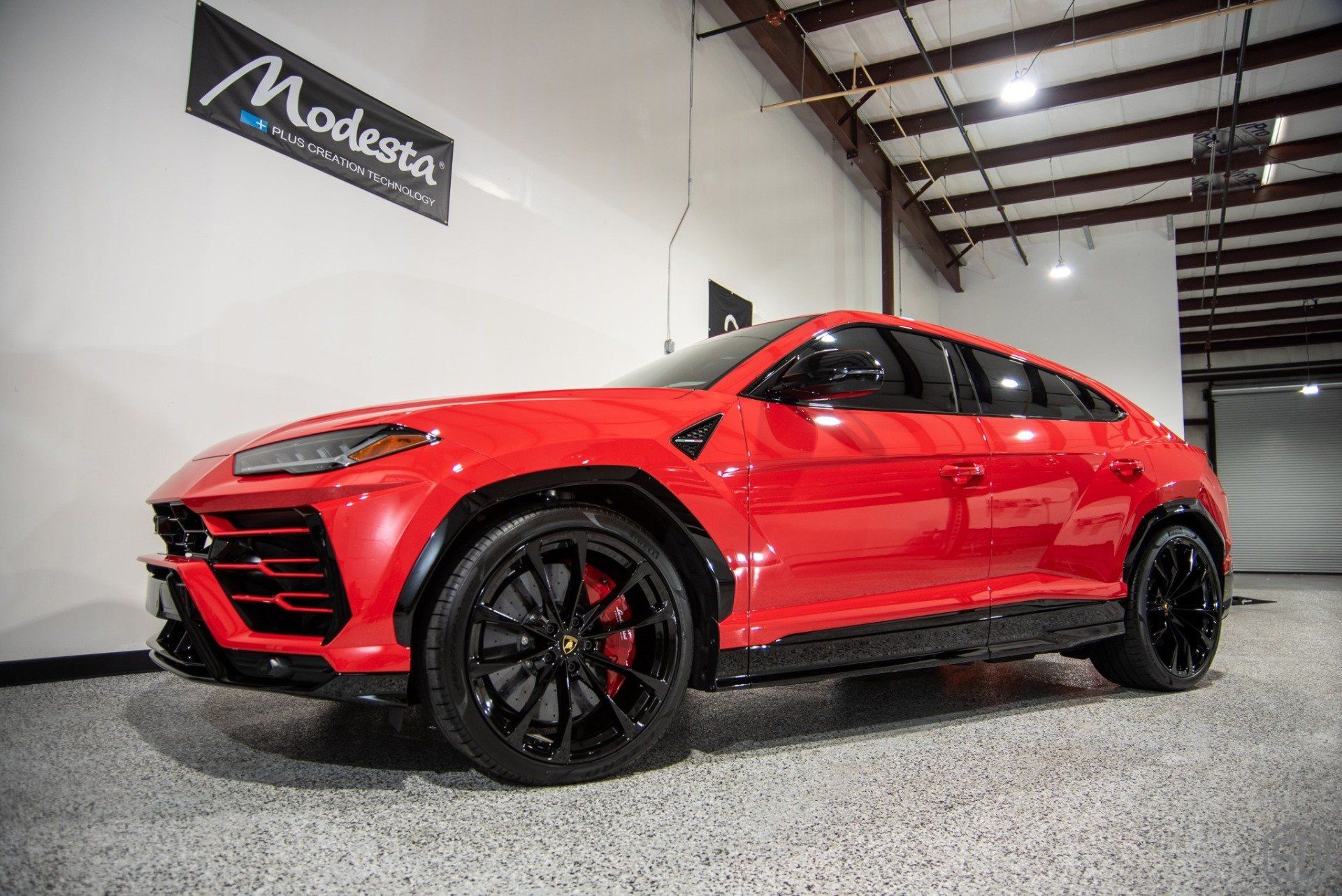 A red lamborghini urus is parked in a garage.