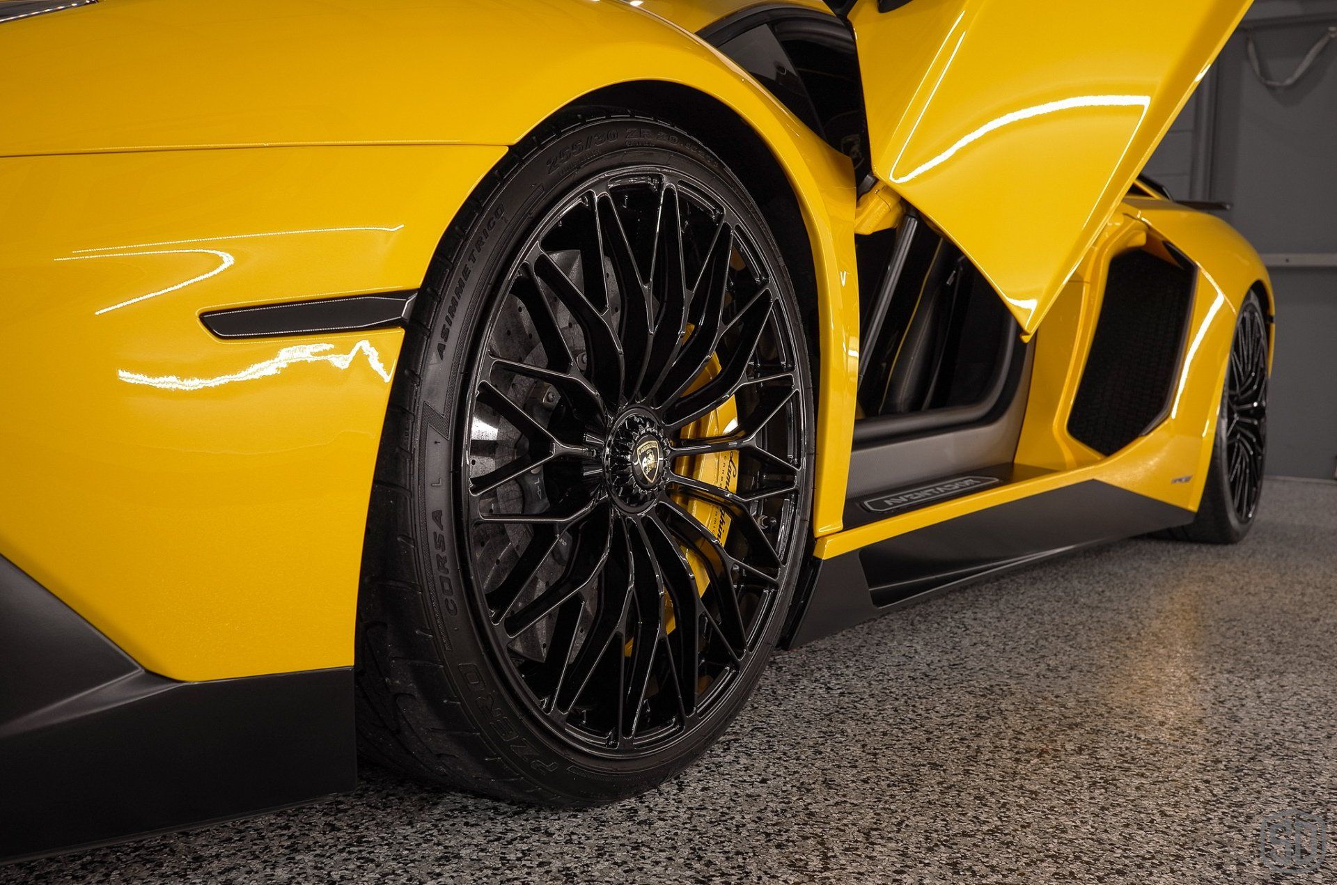 A yellow lamborghini aventador is parked in a garage with its door open.