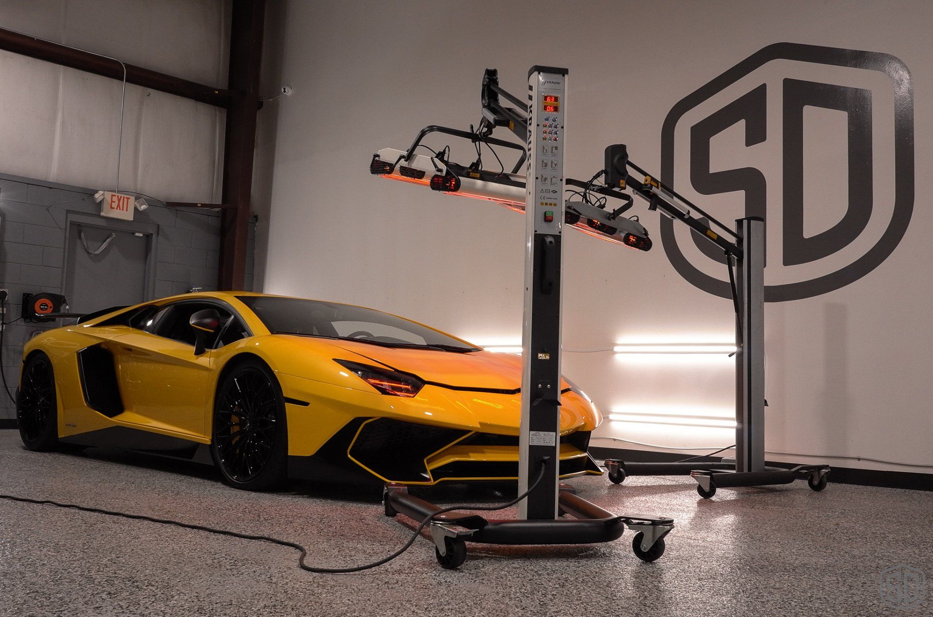 A yellow lamborghini aventador is sitting in a garage next to a sd logo.