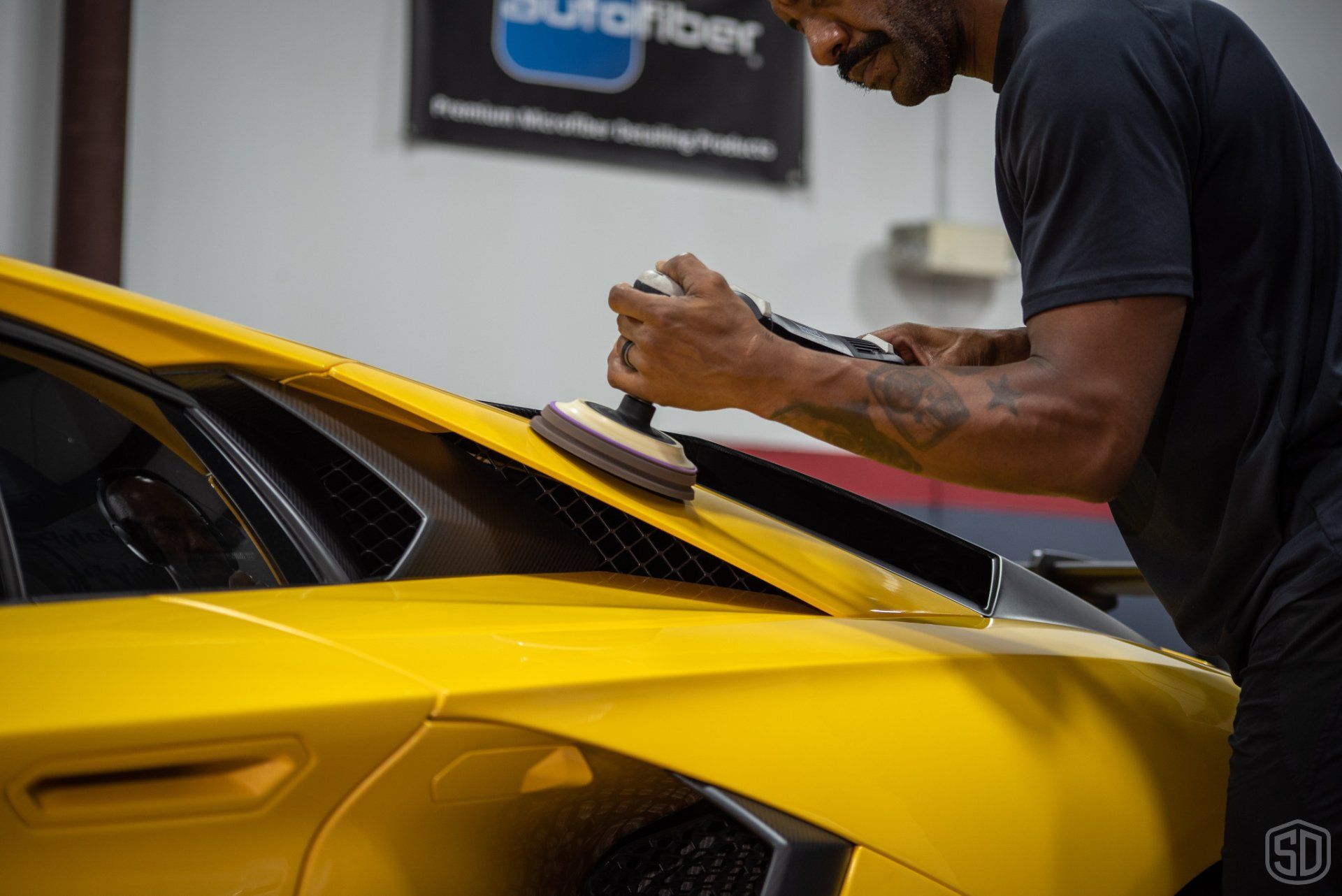 A man is polishing the windshield of a yellow car.