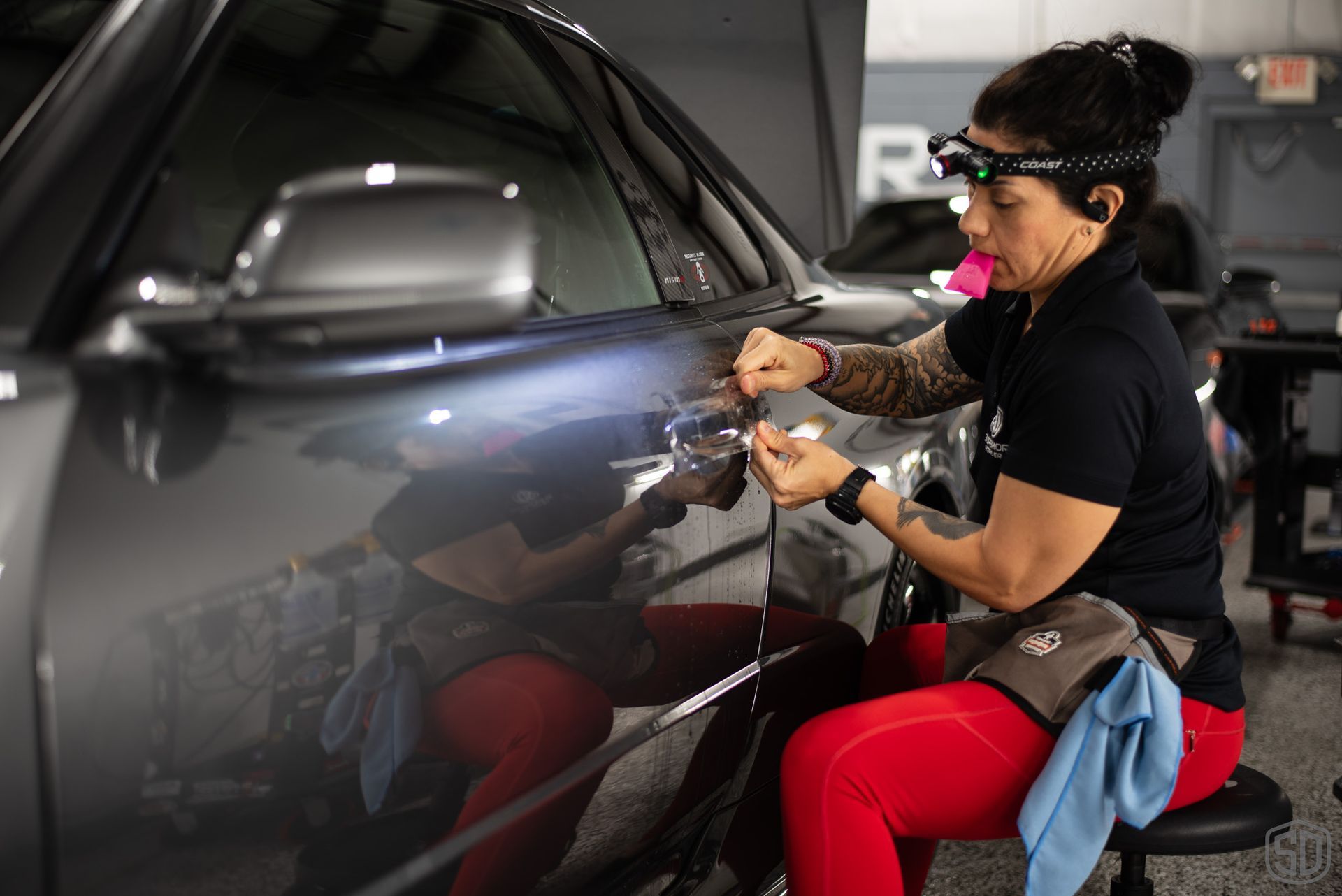 A woman is sitting on a stool working on a car.