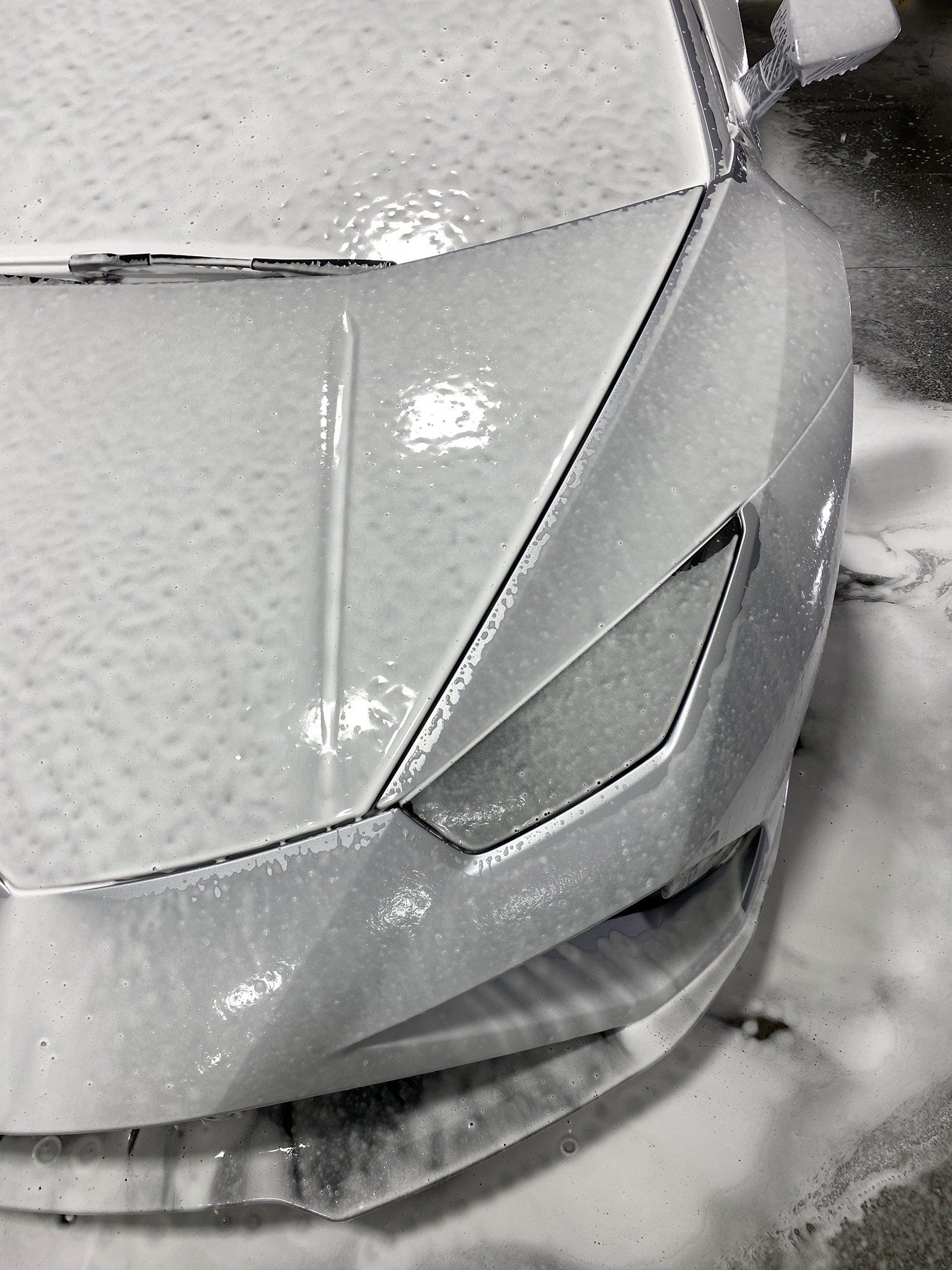 A close up of a white car covered in foam.
