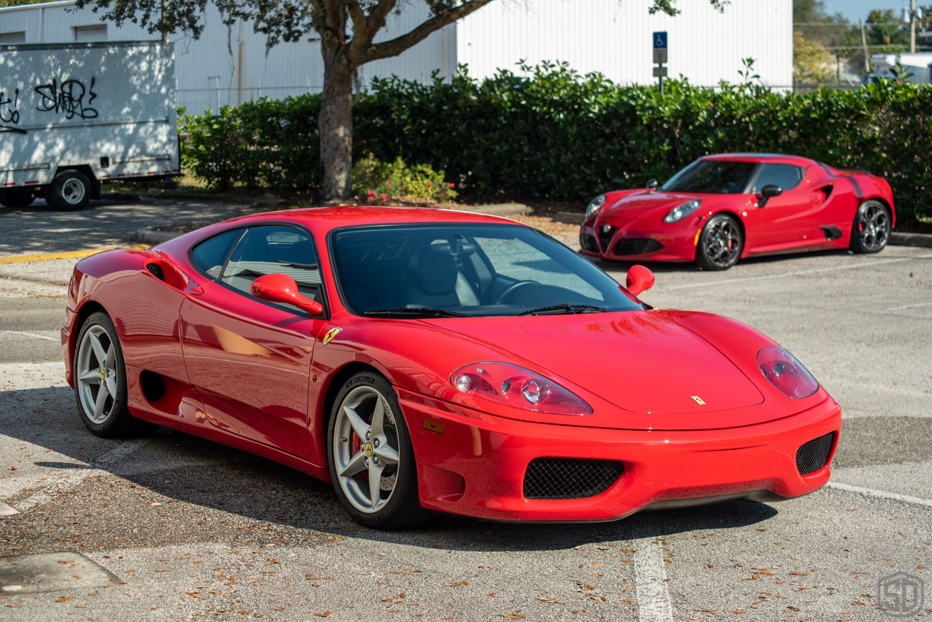 Two red ferraris are parked in a parking lot.