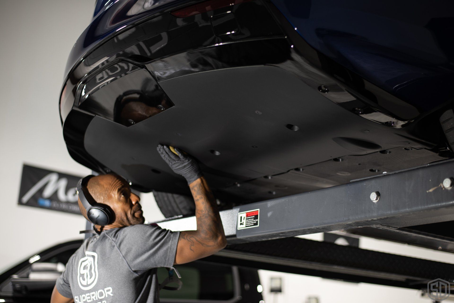 A man wearing headphones is working on the underside of a car.