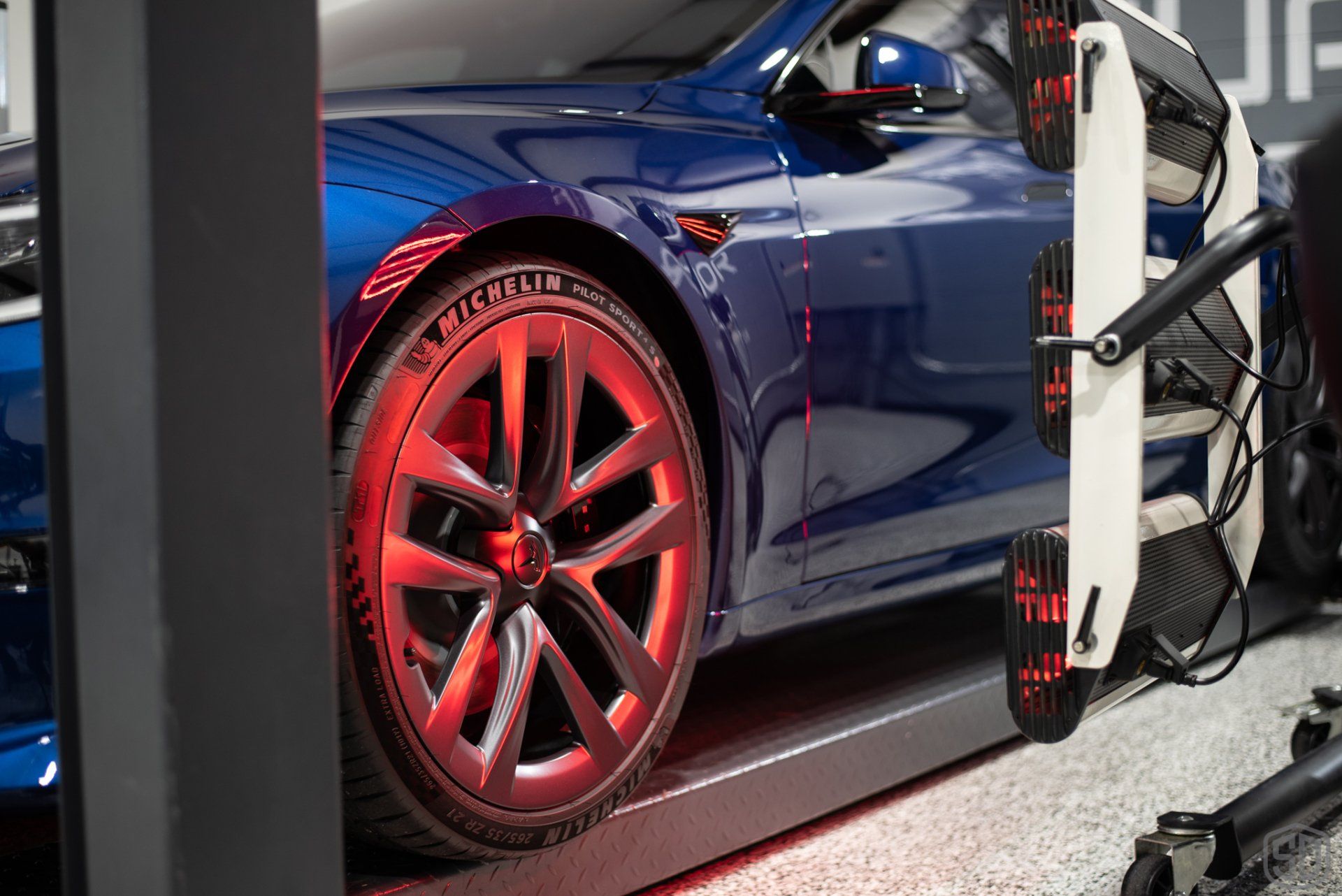 A tesla model s is being tested by a machine in a garage.