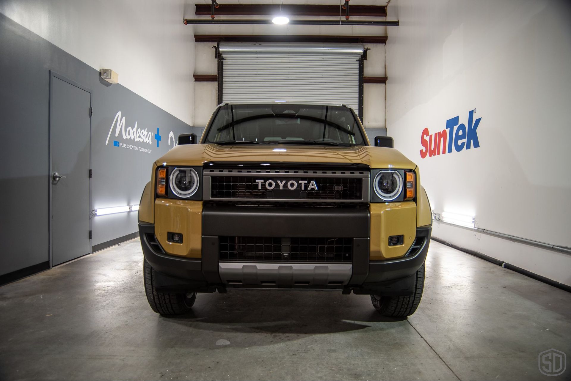 A yellow toyota truck is parked in a garage next to a suntek sign.