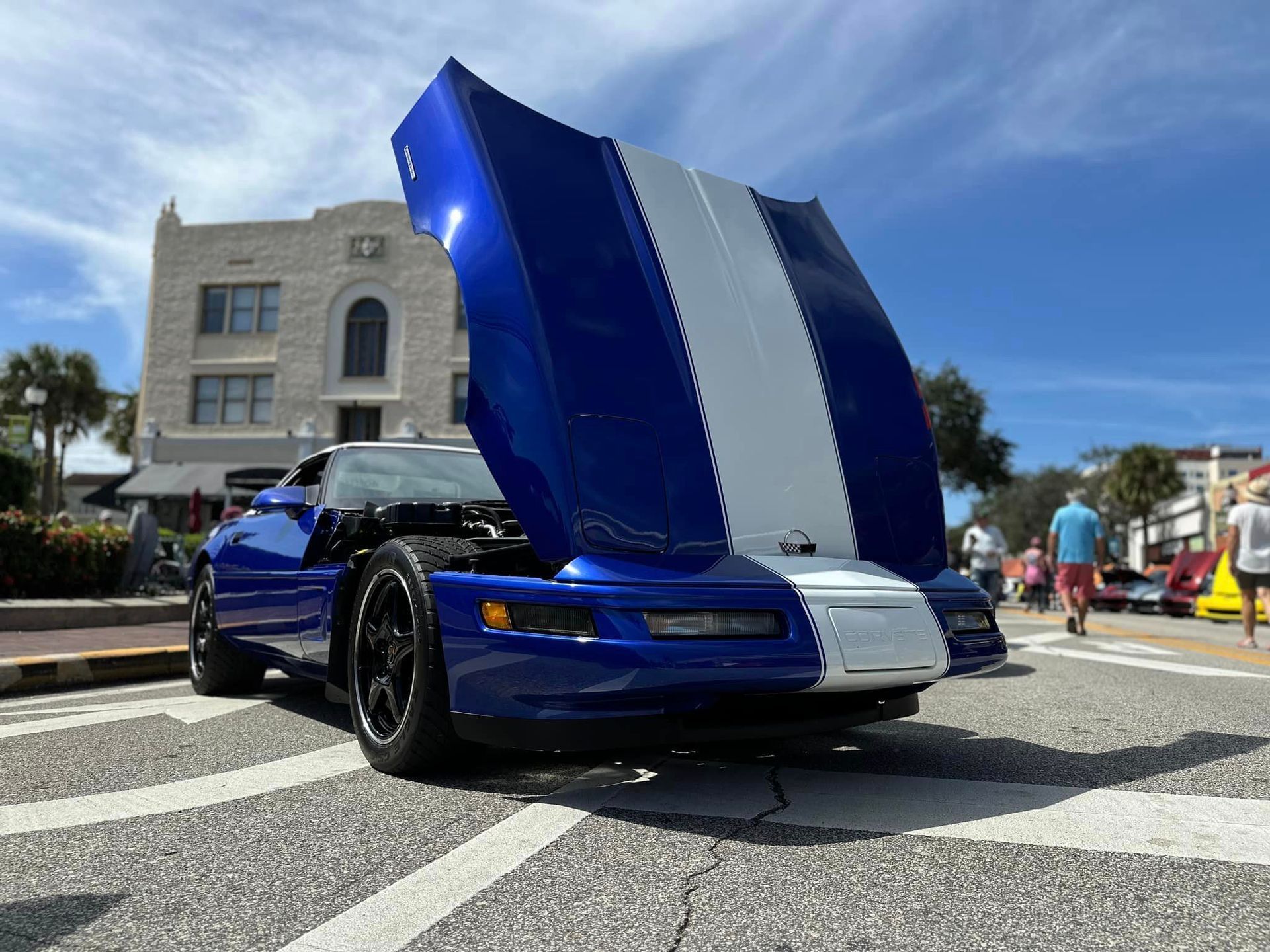 A blue and white sports car with the hood up is parked on the side of the road.