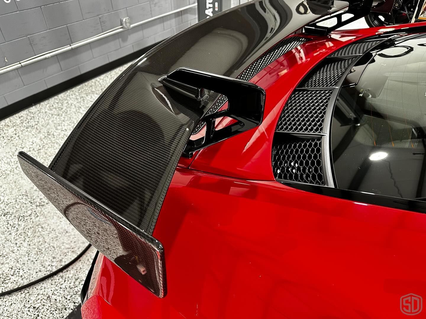 A red sports car with a black wing is parked in a garage.