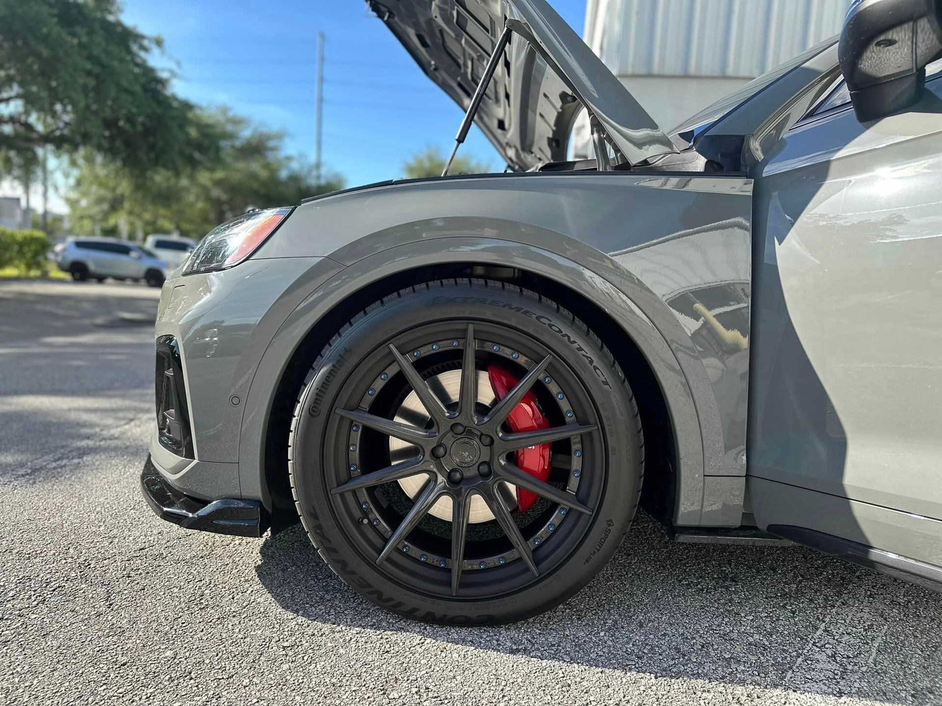 A gray car with the hood up is parked in a parking lot.