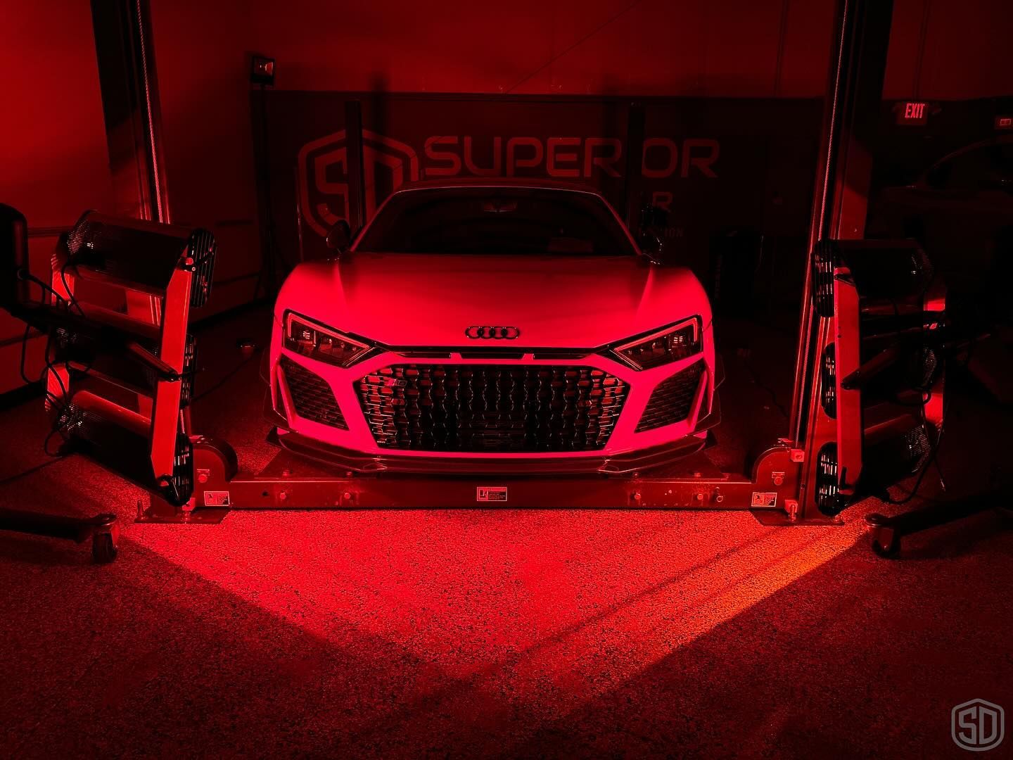 A red car is parked in a garage under red lights.