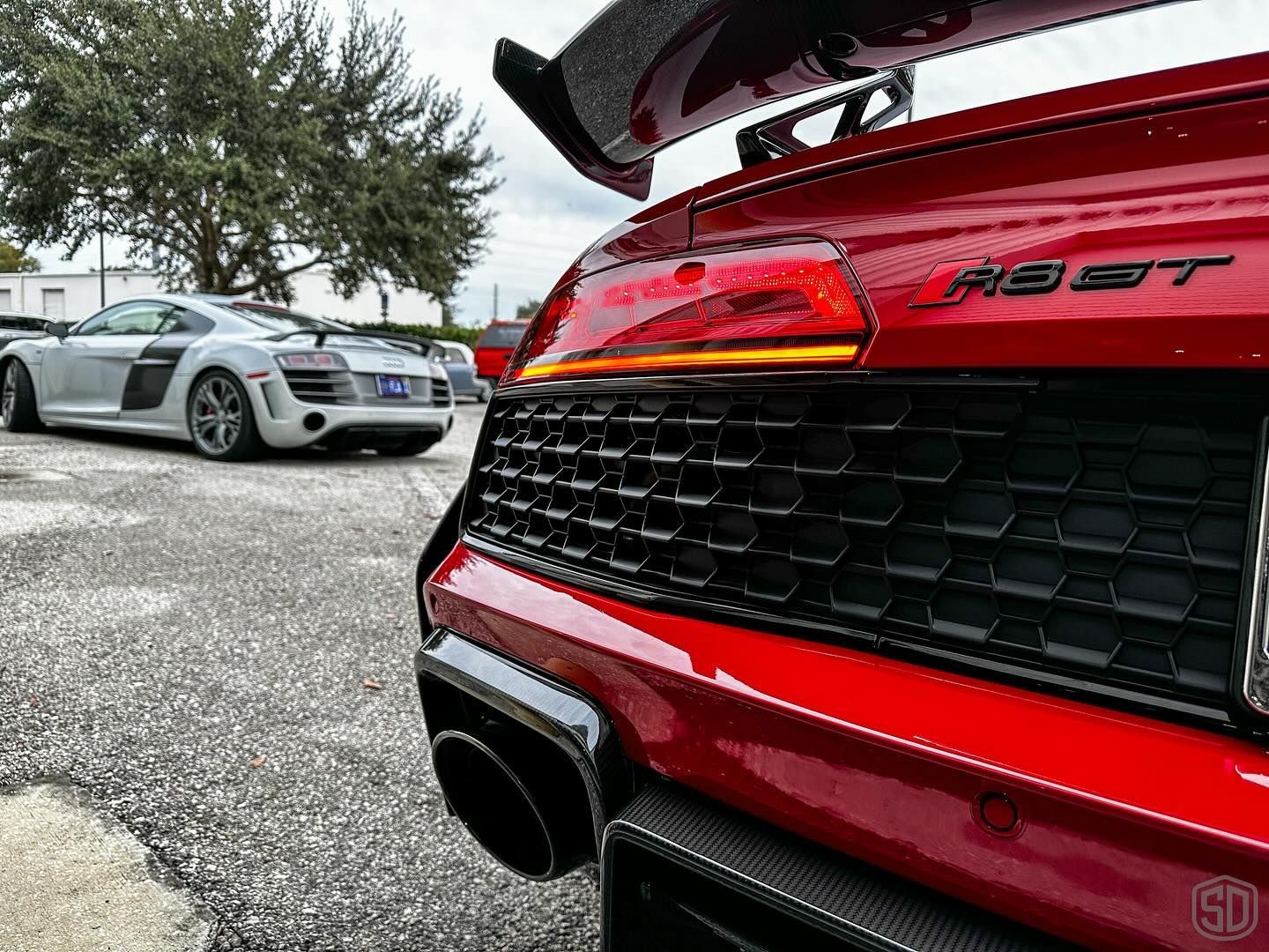 A red audi r8 gt is parked next to a silver audi r8 gt in a parking lot.