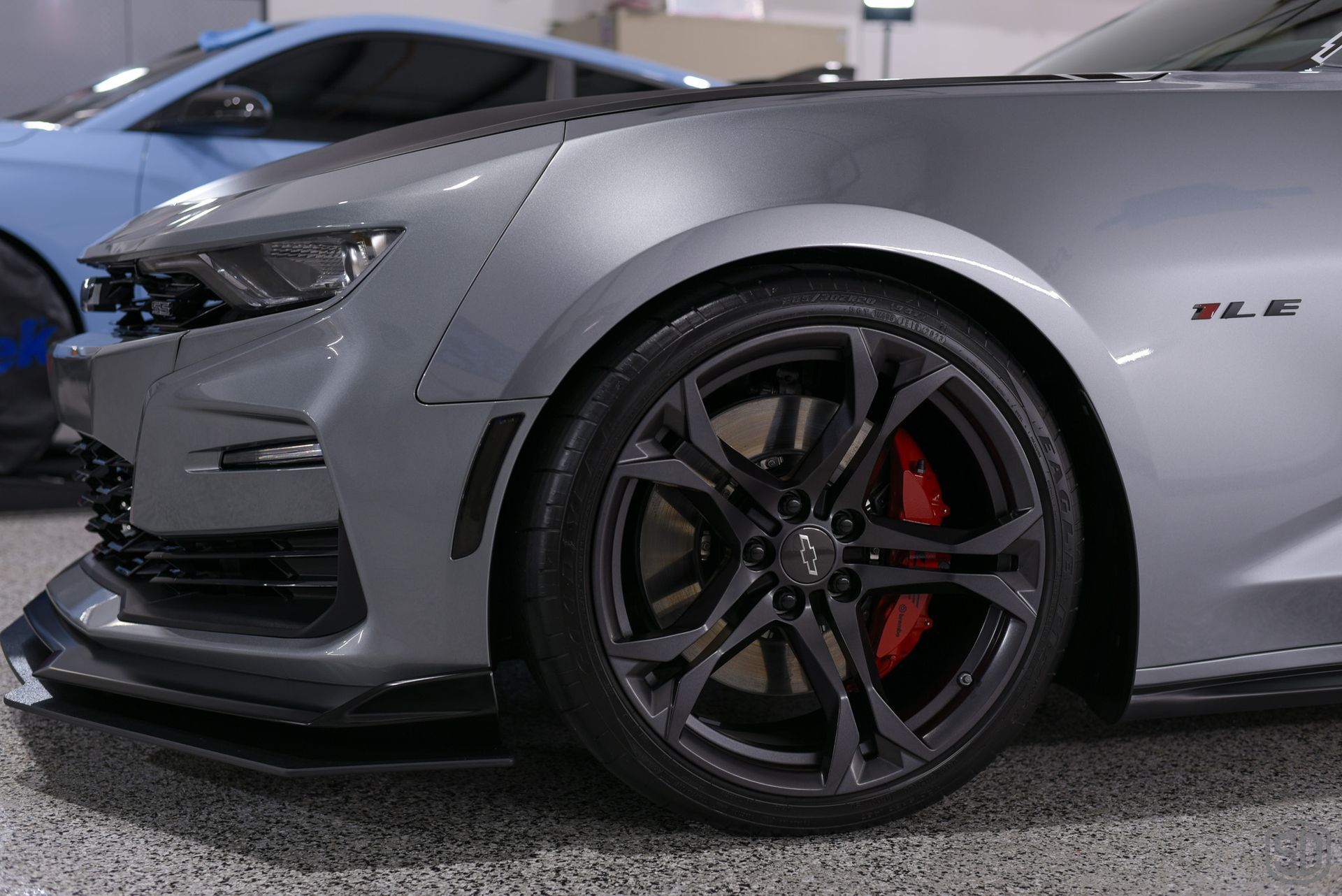 A gray car with red brake calipers is parked in a garage.