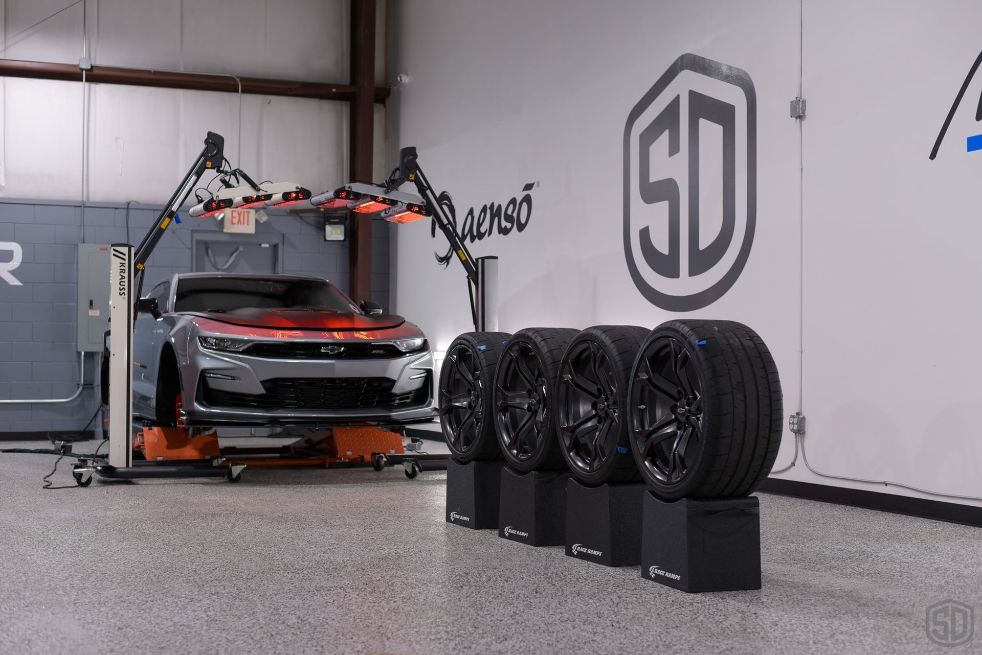 A car is sitting on a lift in a garage next to a row of tires.