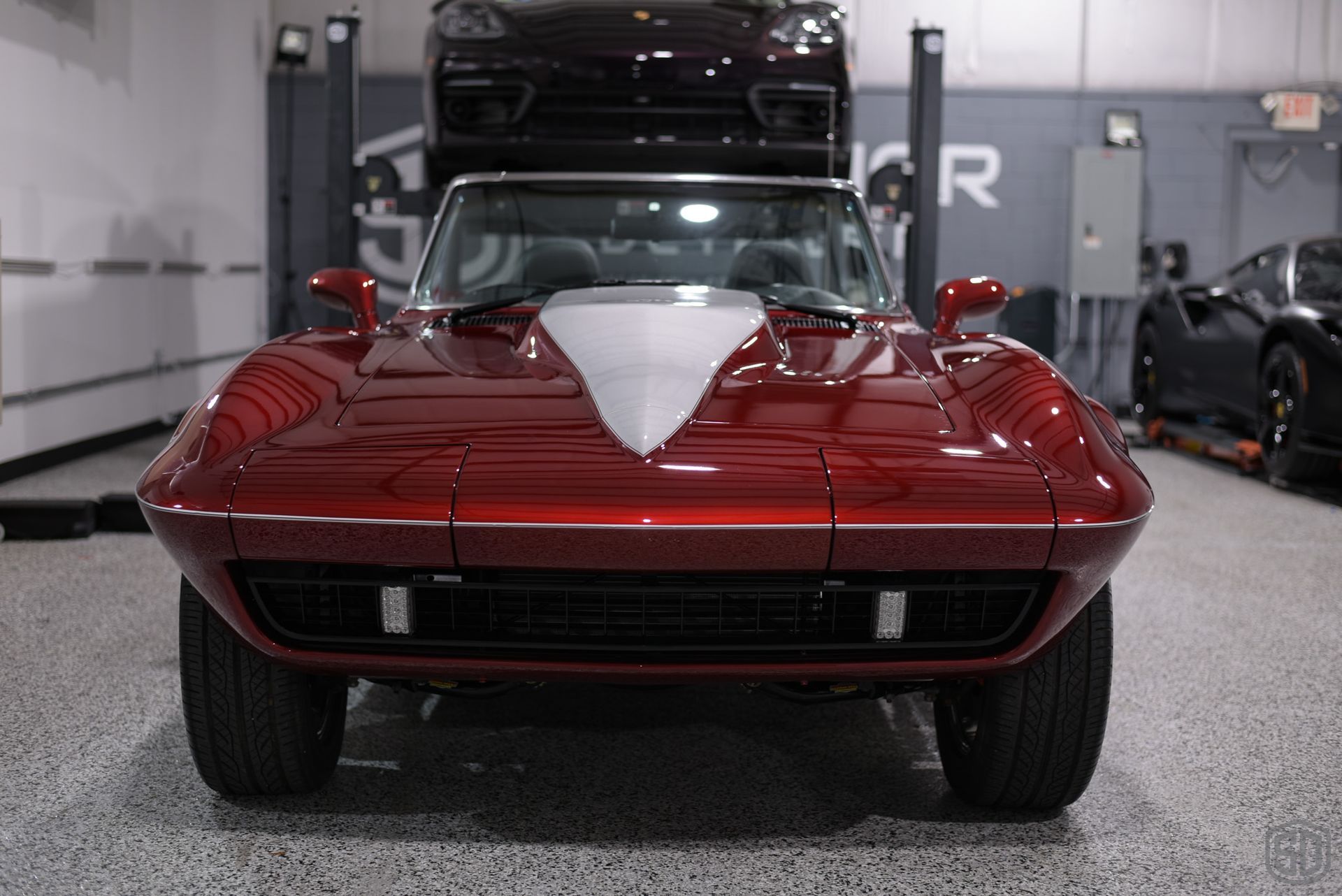 A red corvette is parked in a garage with other cars.