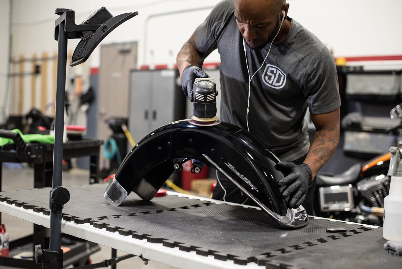 A man is polishing a motorcycle fender in a garage.