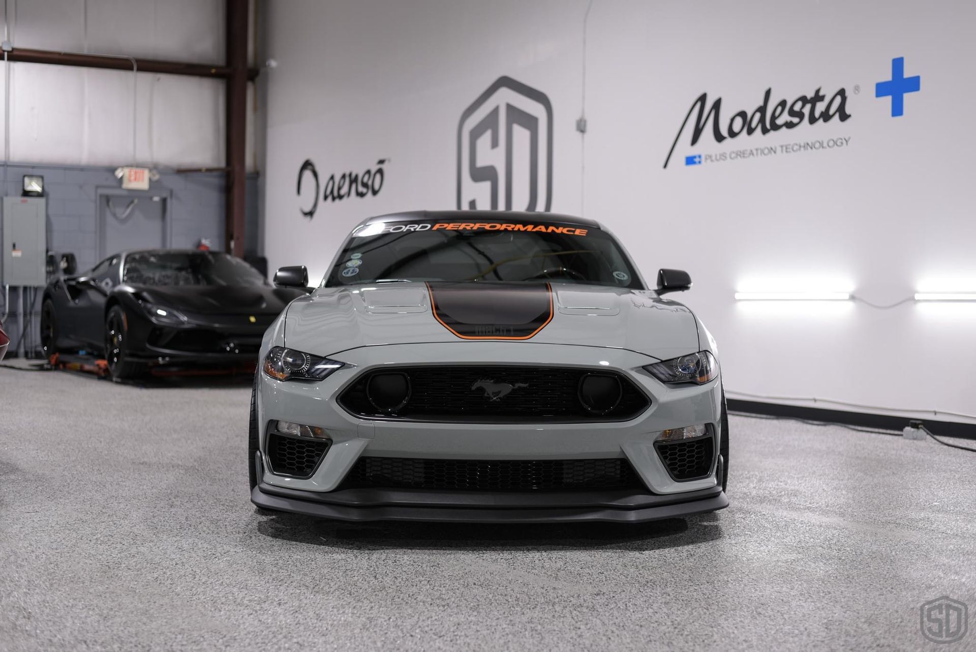 A white mustang is parked in a garage next to a black car.