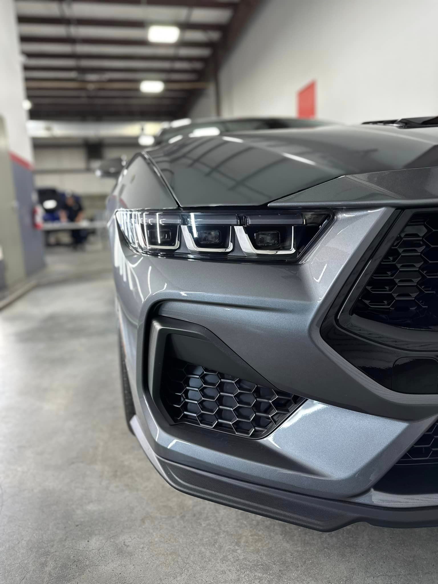 A close up of the front of a gray mustang in a garage.
