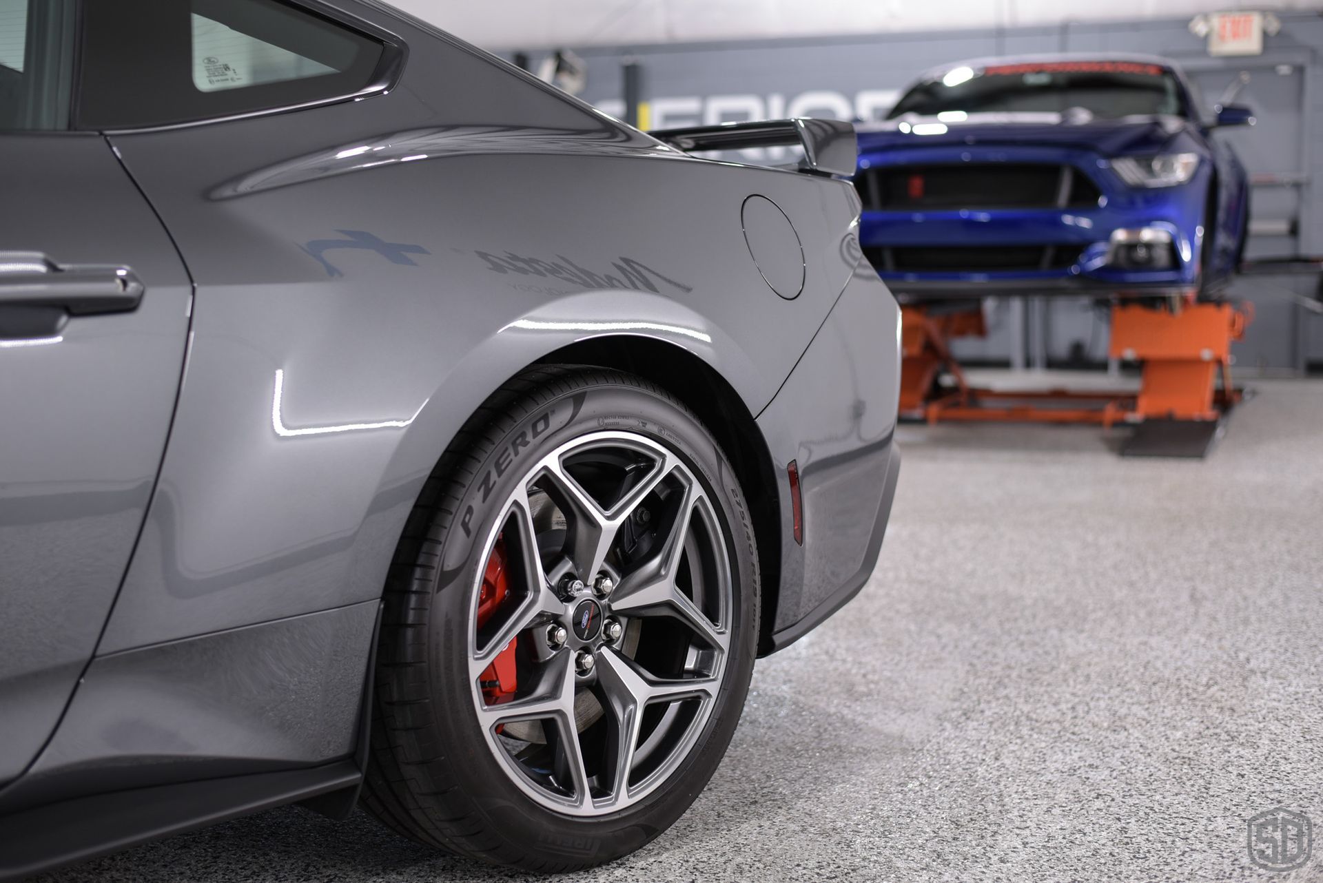A gray mustang is parked in a garage next to a blue mustang.
