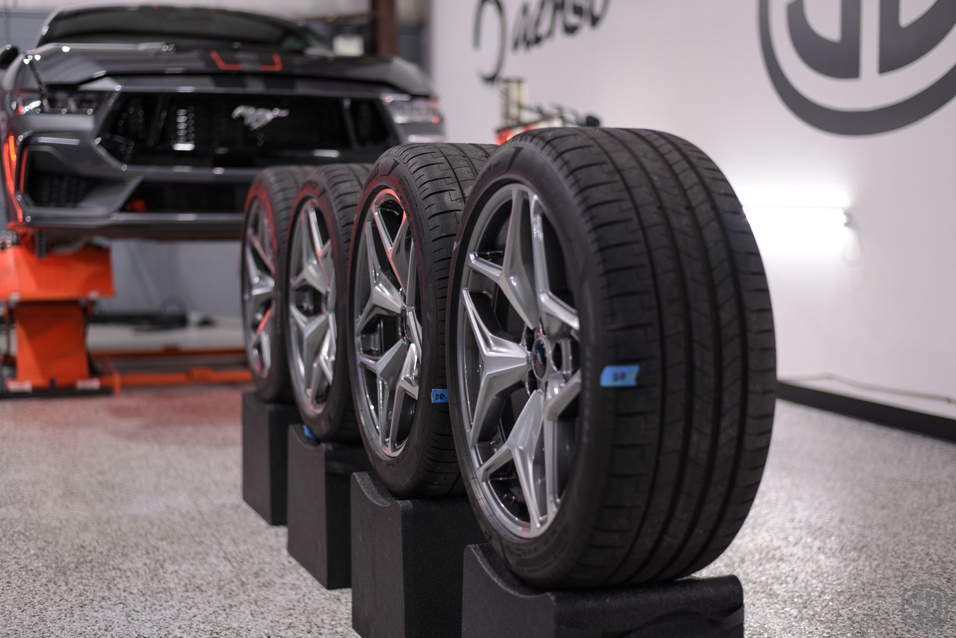 A row of tires are sitting on blocks in front of a mustang.